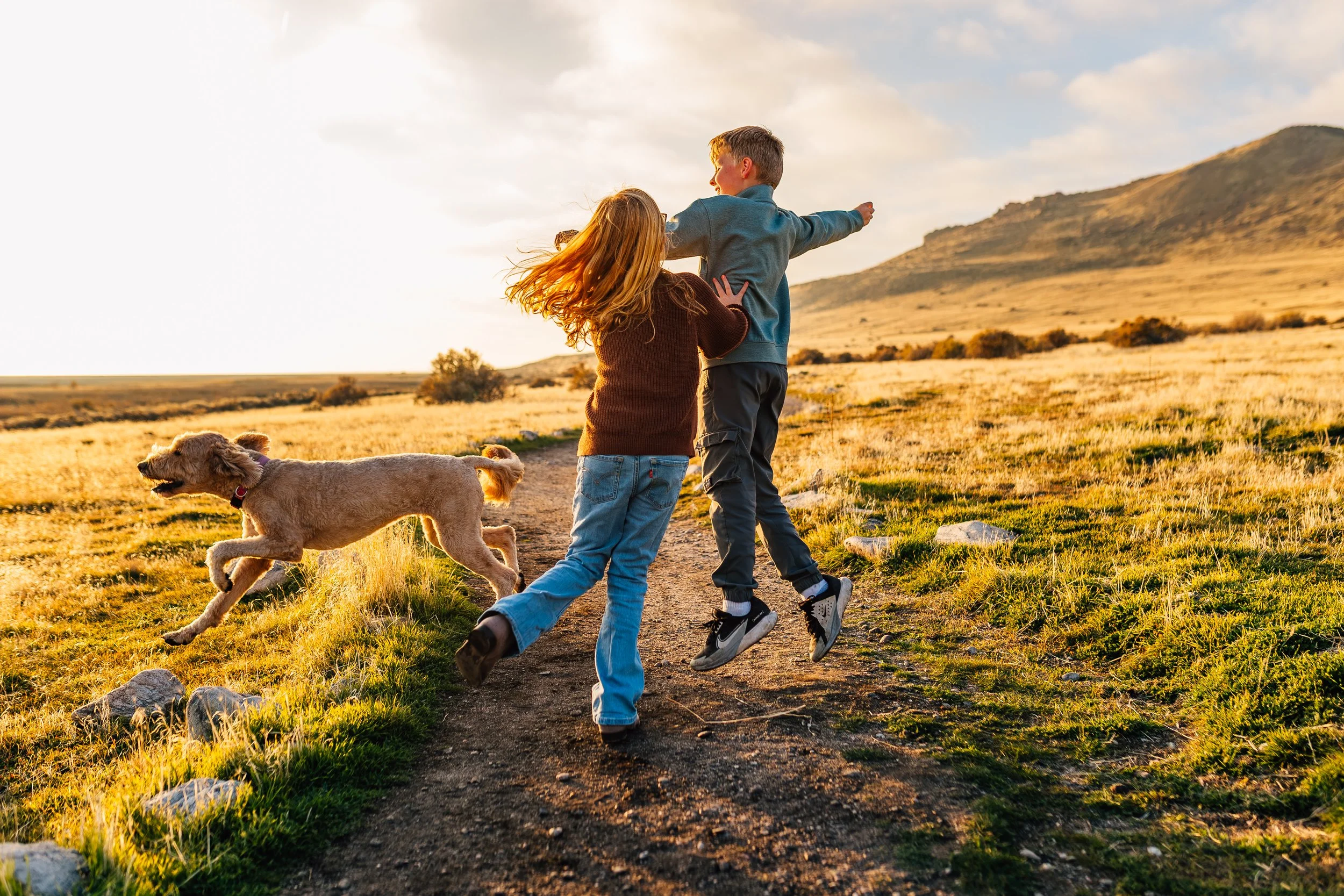 Candid documentary family photo of children playing with their dog during an outdoor session in Northern Utah, captured in natural light