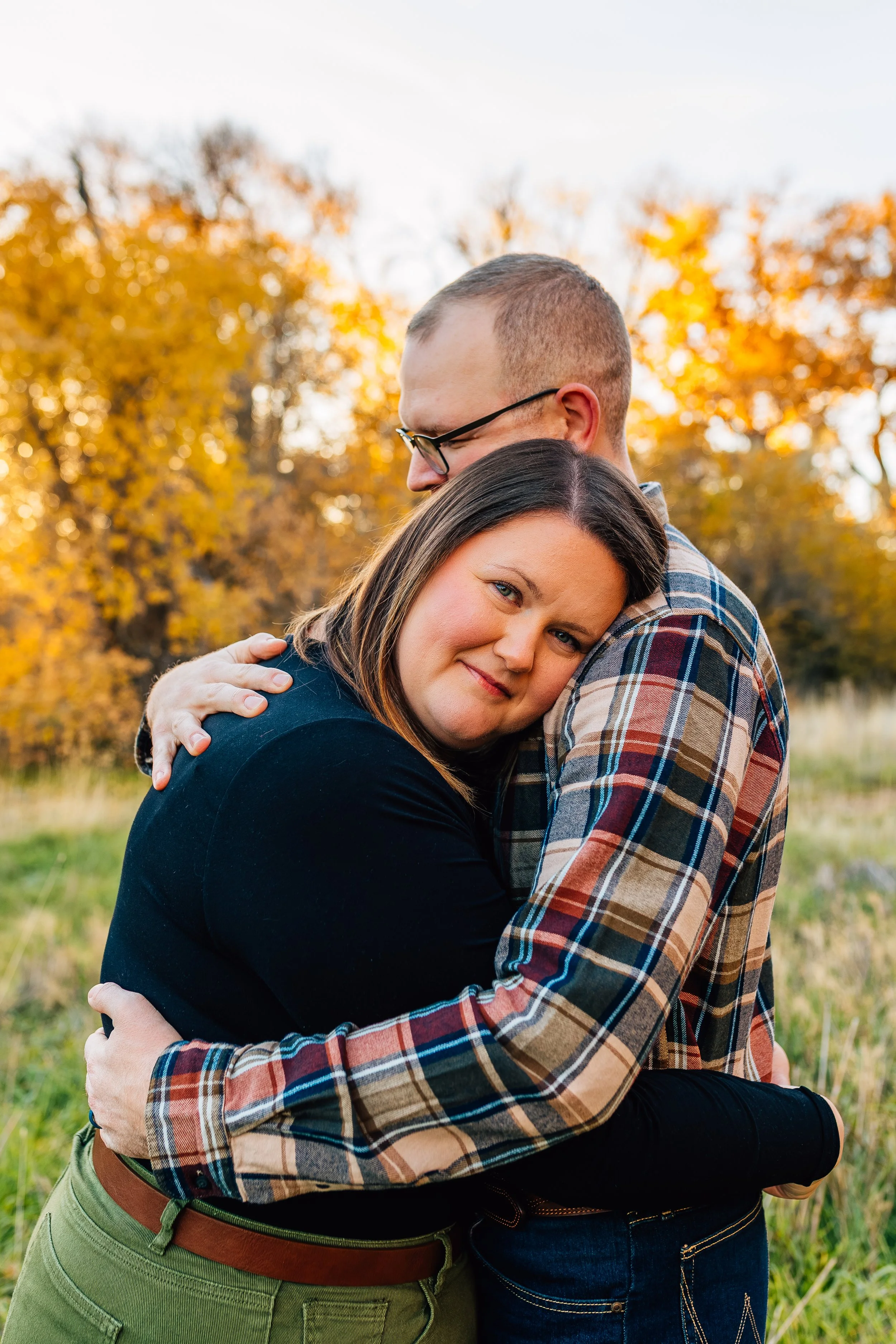 A couple hugging outdoors during fall with colorful autumn trees in the background.