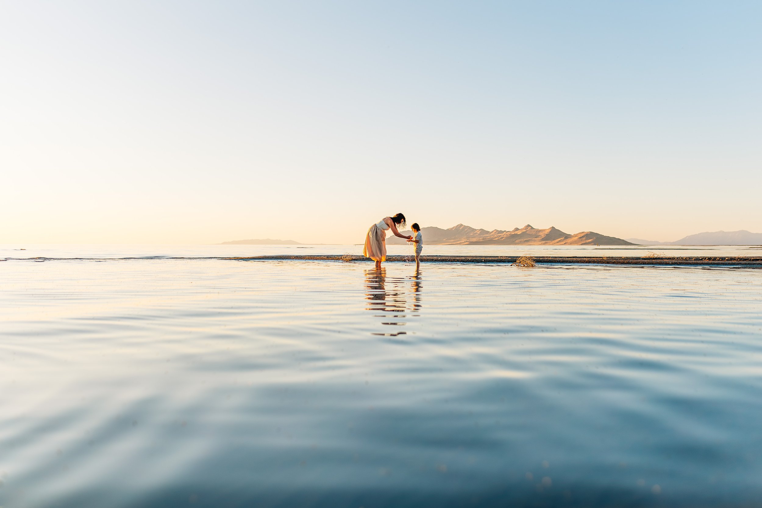 A parent and child standing together in shallow water at the Great Salt Lake in Utah during a family photography session