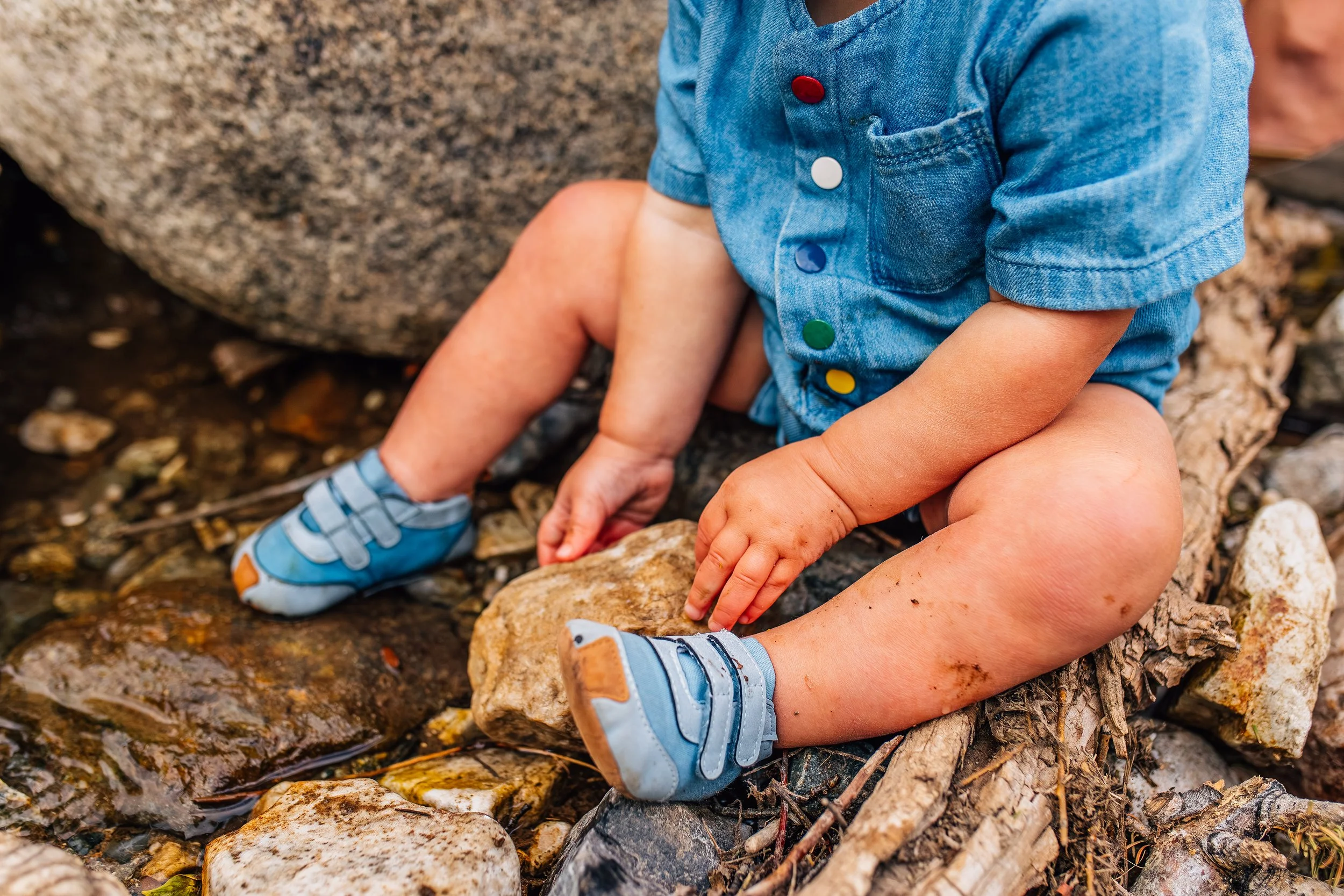 Close-up of a toddler sitting on rocks during a documentary-style child photography session in Weber County, Utah, capturing natural outdoor play without showing the child’s face.