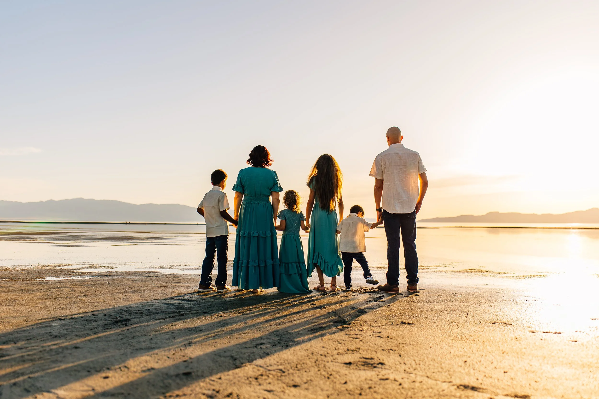 A family of seven holding hands and walking on a beach at sunset.