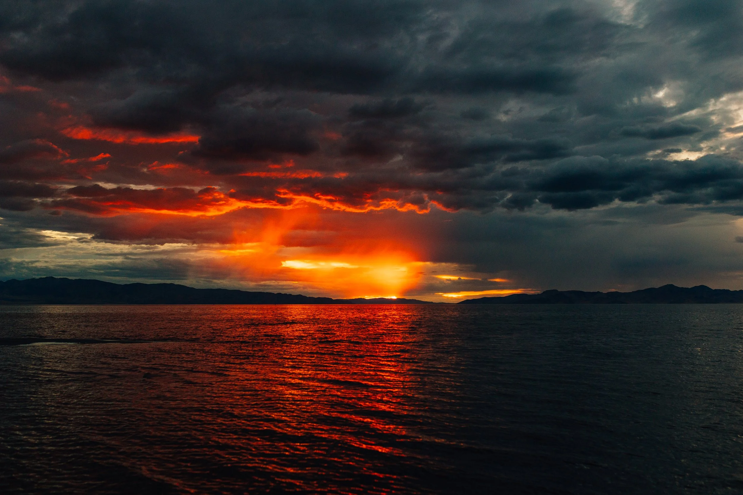 A dramatic sunset over the Great Salt Lake in Utah with dark storm clouds and orange light reflecting on the water
