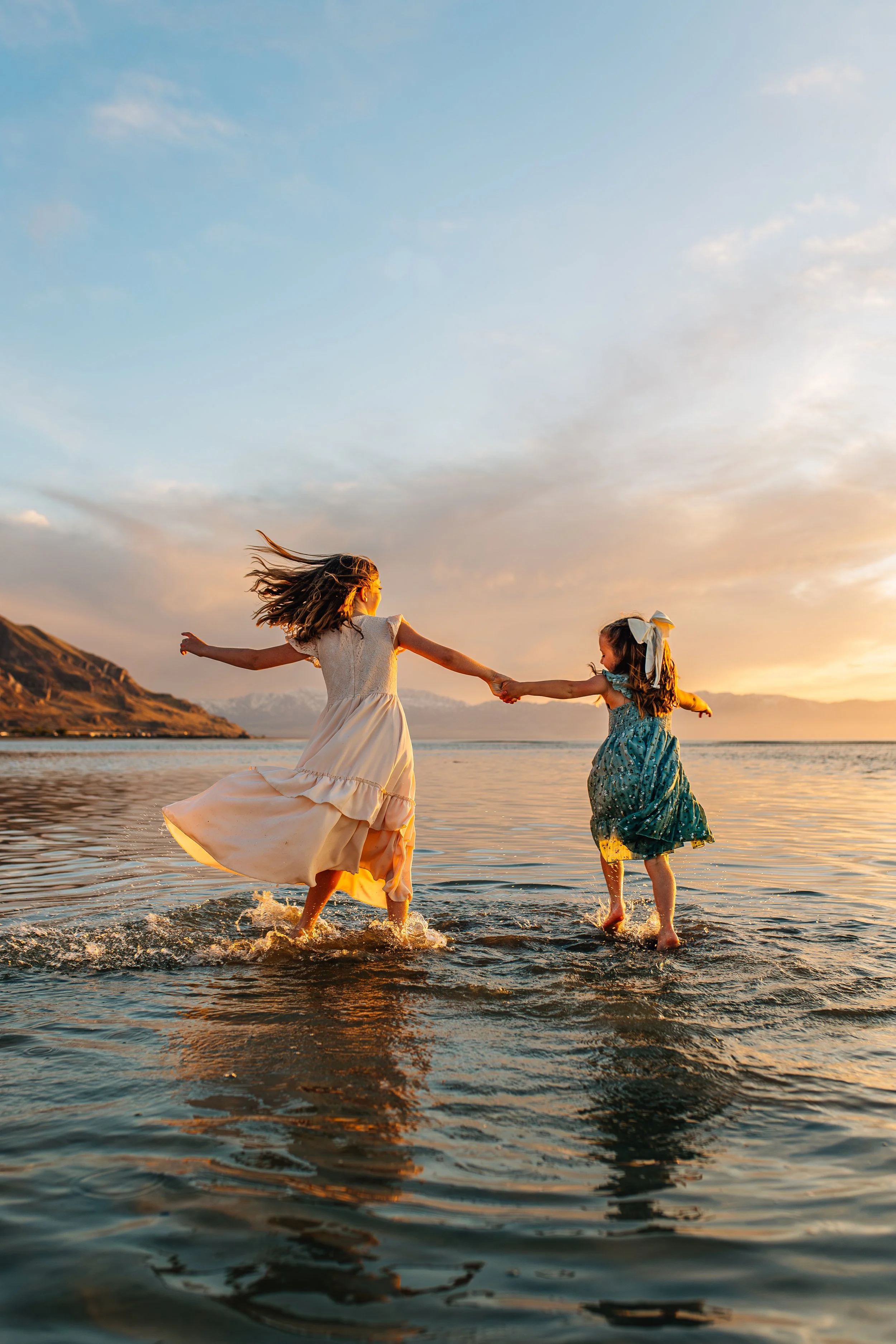 Two girls playing and holding hands in shallow water at sunset.
