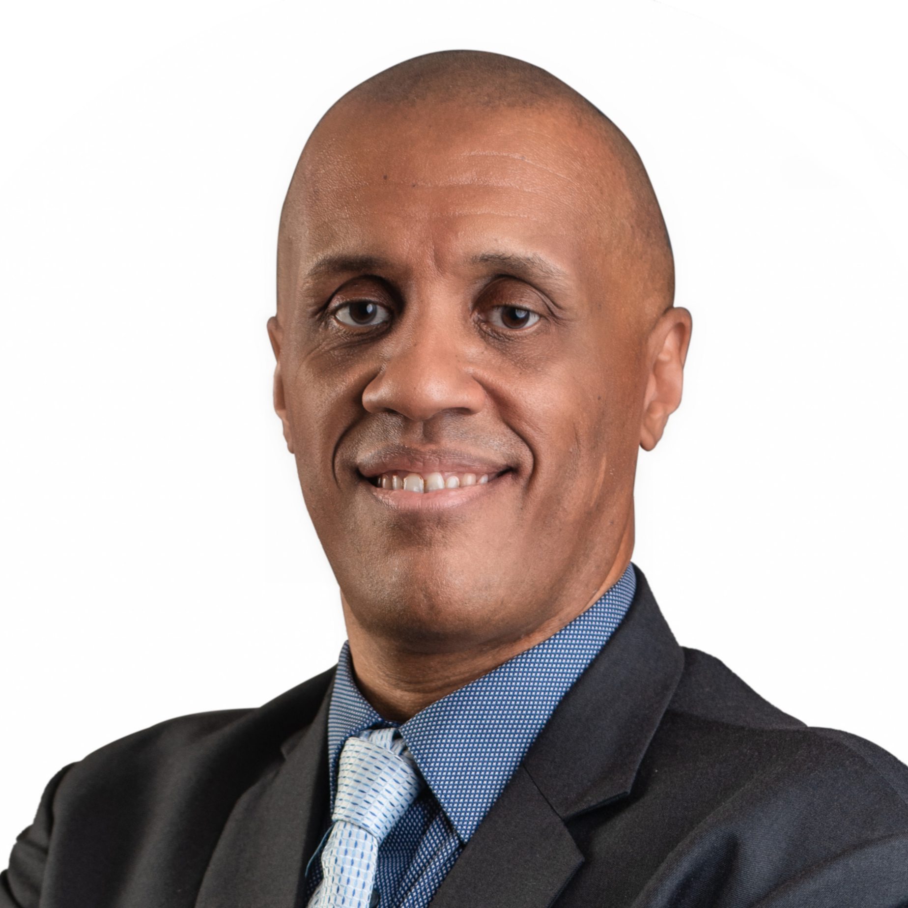 Close-up of a man wearing a dark suit, blue shirt, and patterned tie, with his arms crossed, on a white background.