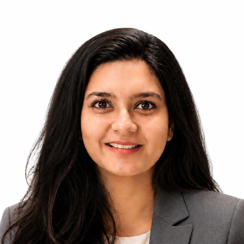 Portrait of a woman with long dark hair, smiling, wearing a gray blazer and white shirt, against a white background.