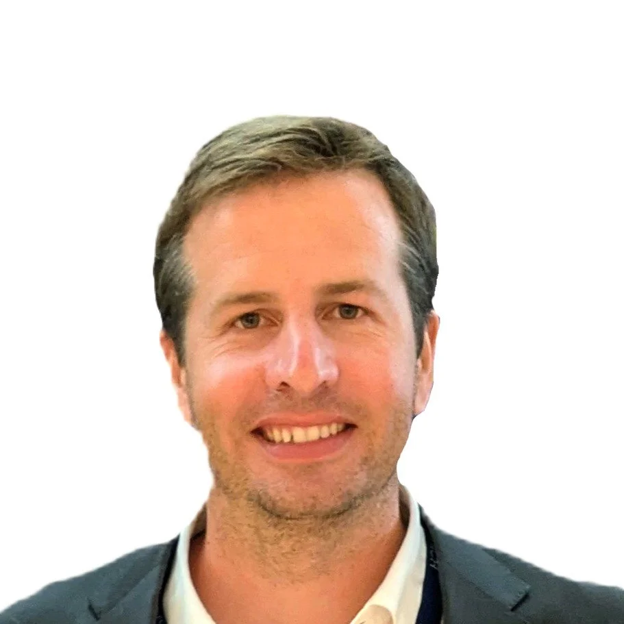 Headshot of a smiling man with brown hair, wearing a dark suit jacket and white collared shirt, against a plain white background.