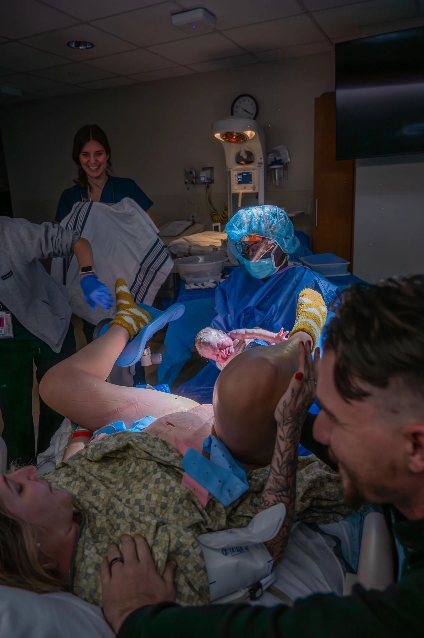 A woman in labor holding her newborn baby in a hospital delivery room with medical staff present.