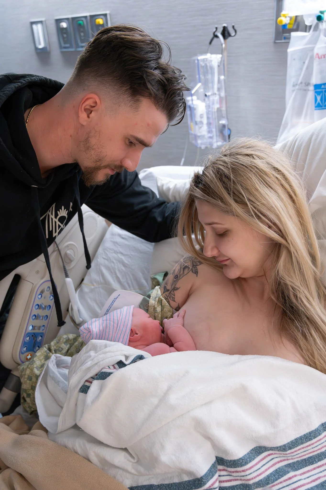 A woman holding a newborn baby and a man leaning over her in a hospital room.