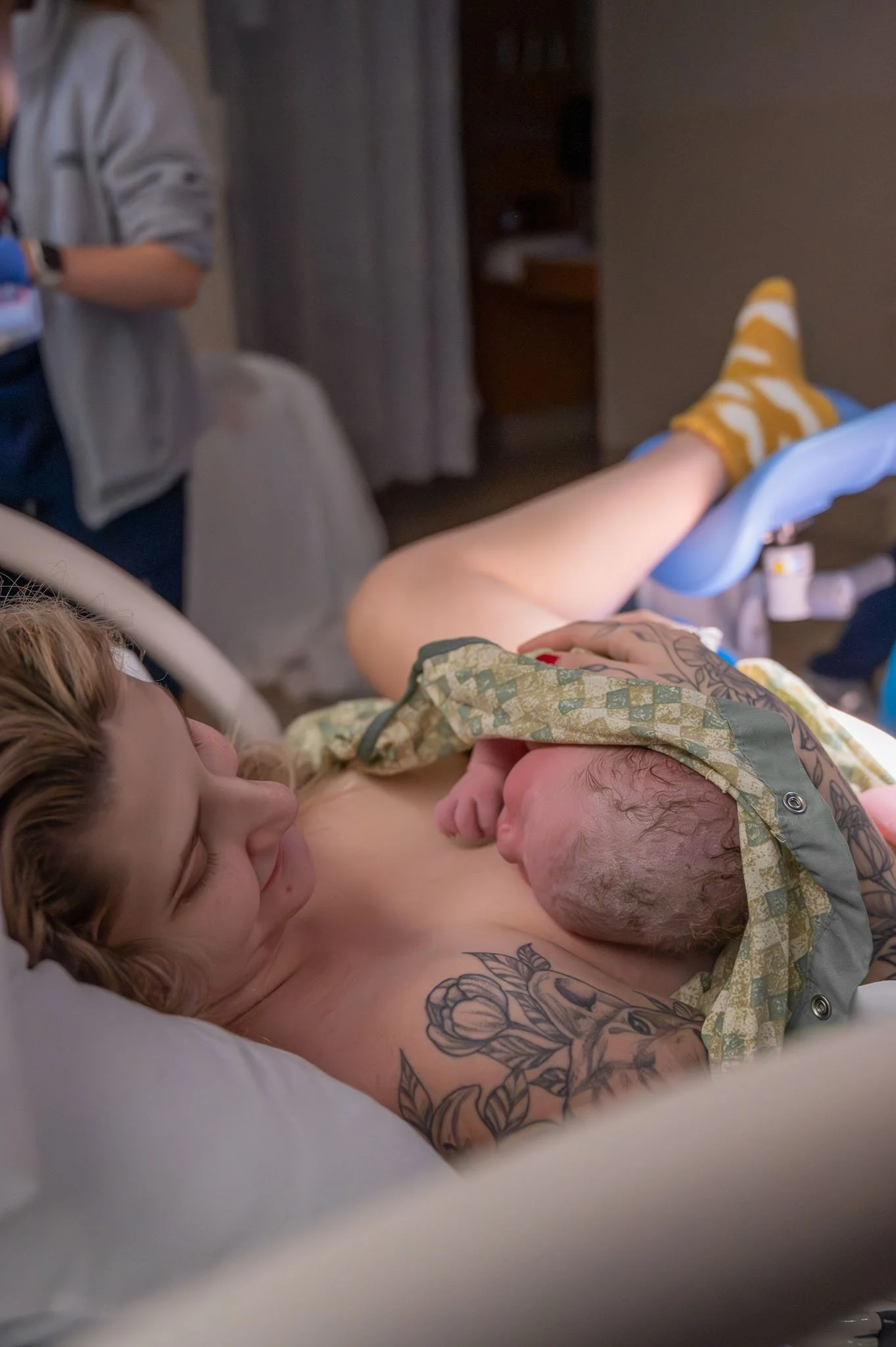 A woman lying in a hospital bed holding a newborn baby against her chest.