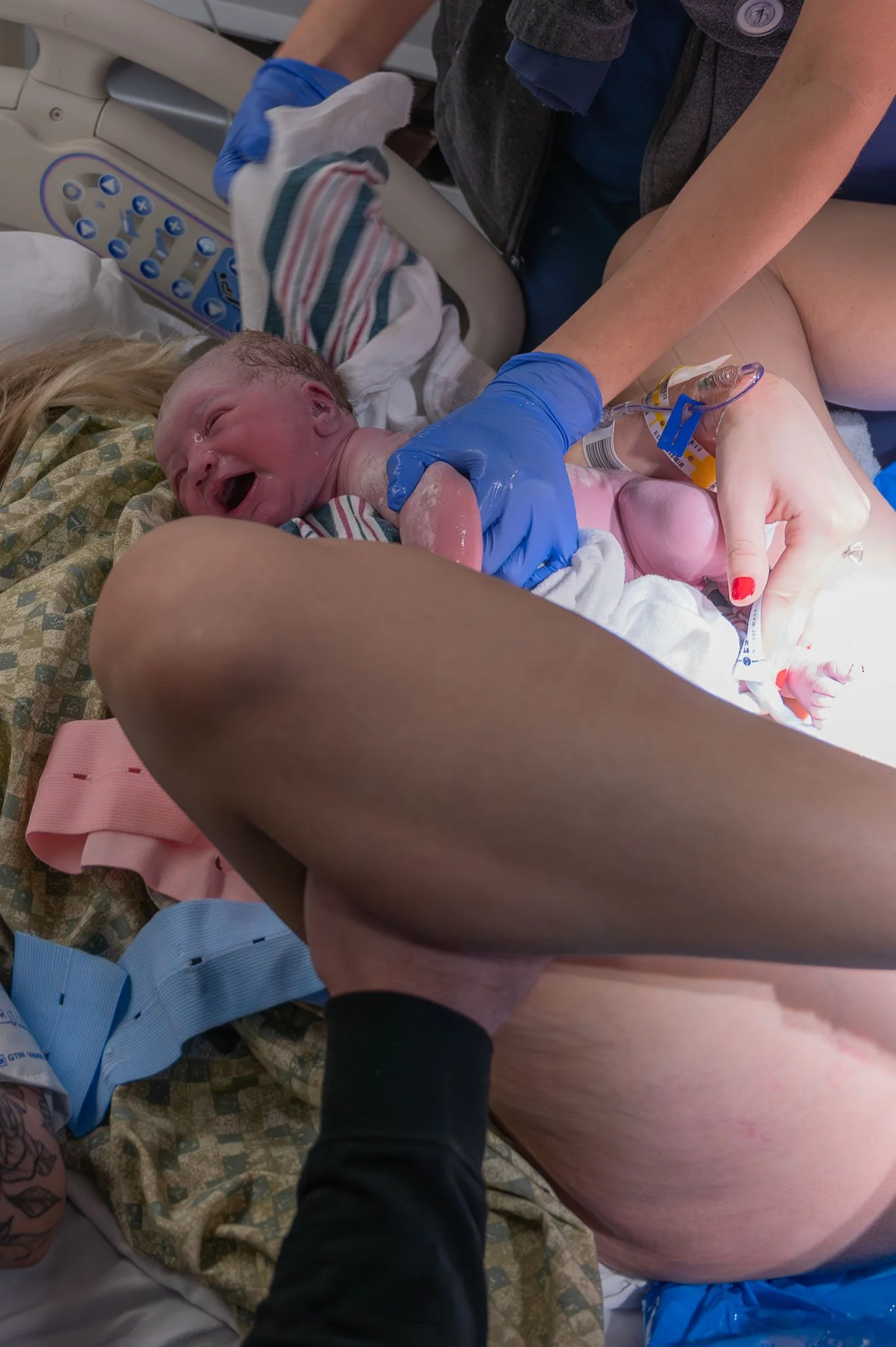 Newborn baby being delivered into the world during birth in a hospital, with medical professionals assisting.