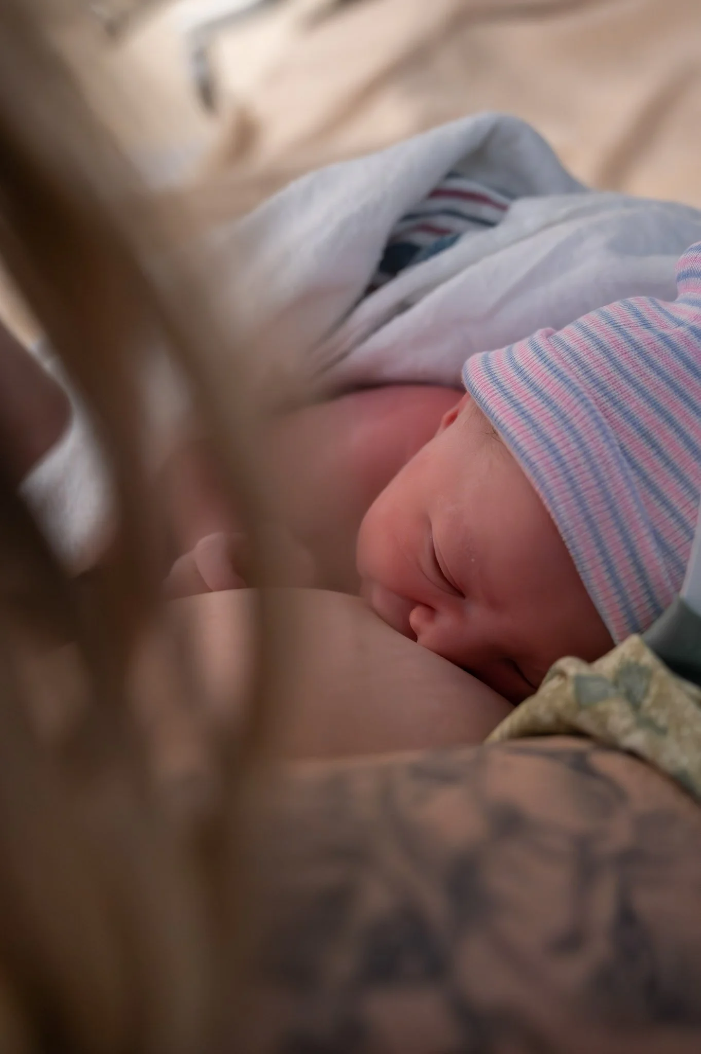 A person breastfeeding a newborn baby, who is wearing a striped hat, lying on their side.