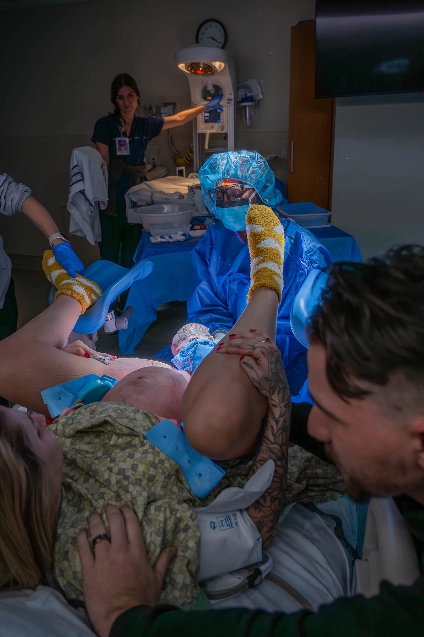 A medical team assisting a woman in labor during childbirth in a hospital room, with doctors, nurses, and medical equipment present.