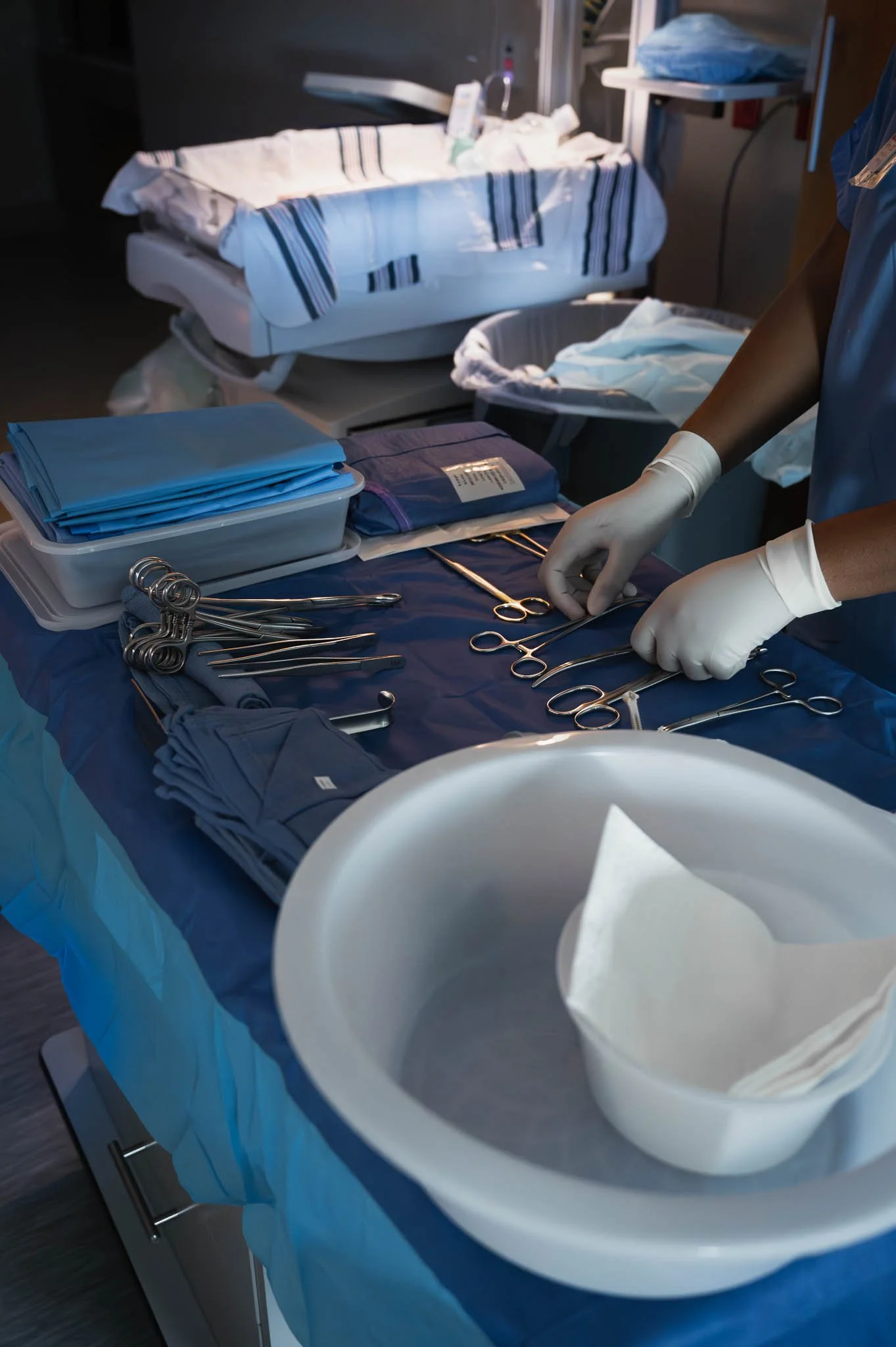 Surgical instruments and supplies on an operating table in a hospital room, with a nurse preparing medical tools.
