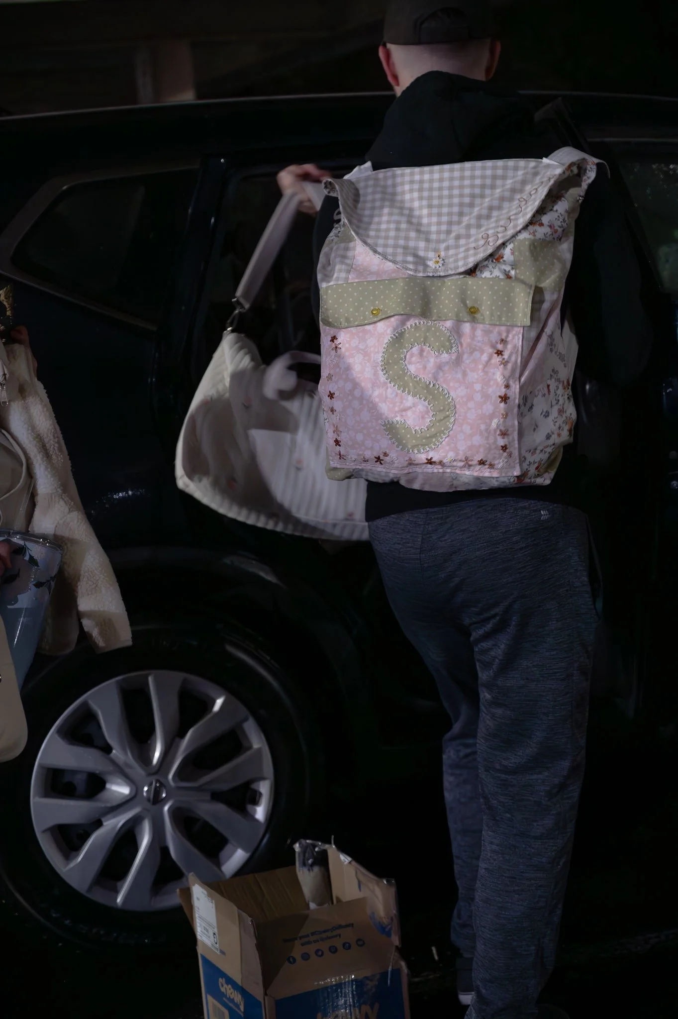 Person loading bags into the back of a black SUV during evening or night.