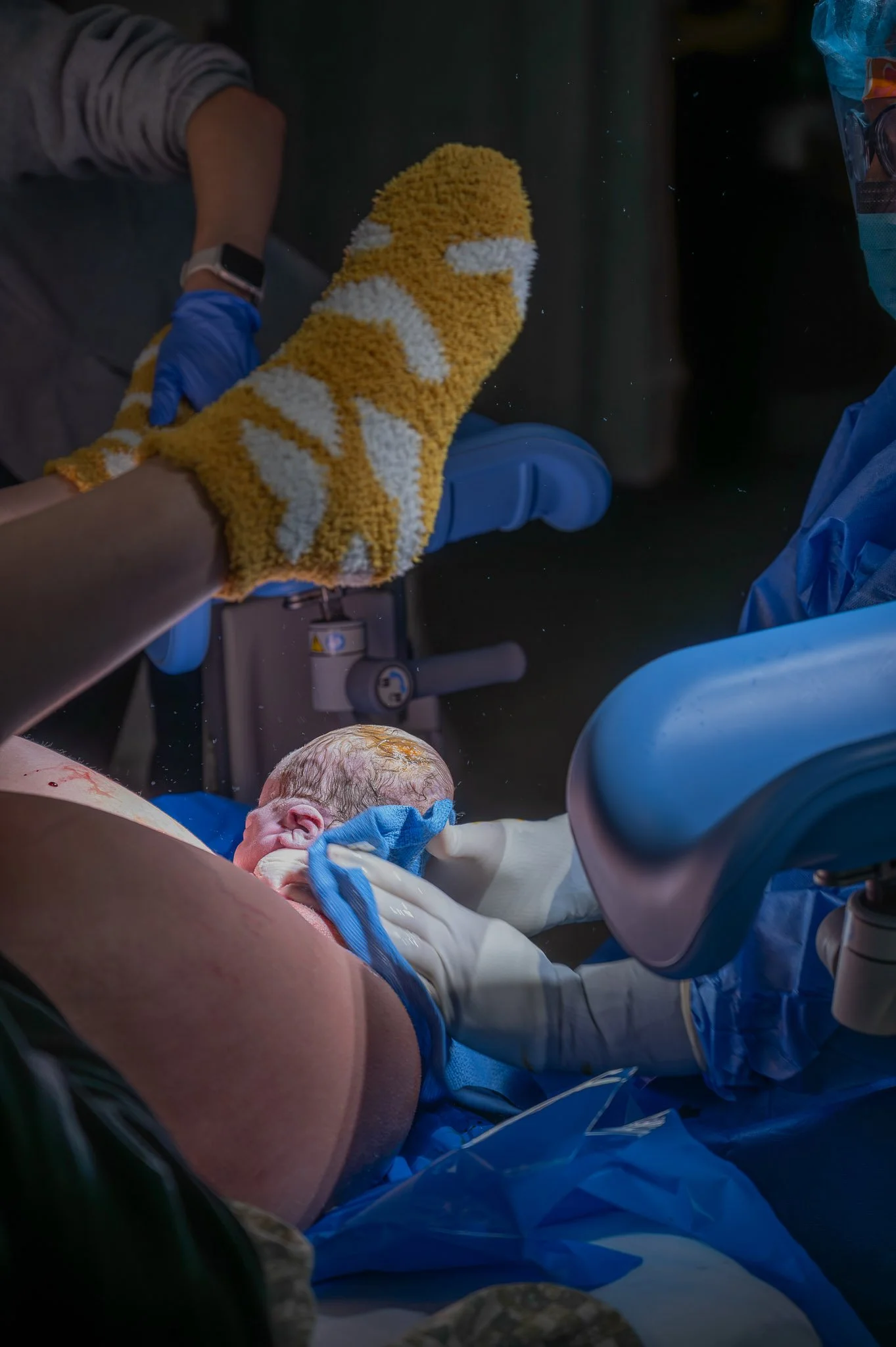 A healthcare professional wearing gloves and a blanket with a dog pattern attends to a newborn baby in a medical setting.