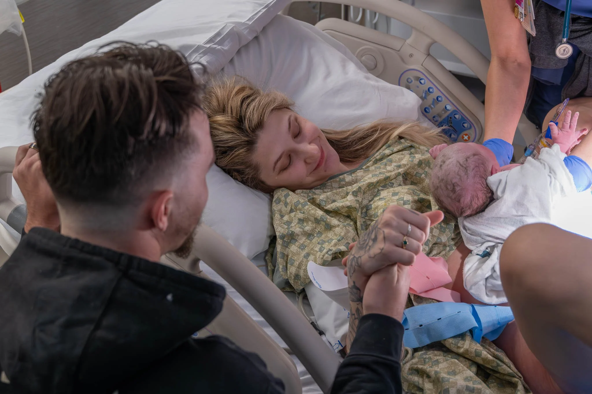A woman in a hospital bed holding a newborn baby, with a man and a nurse attending to them.