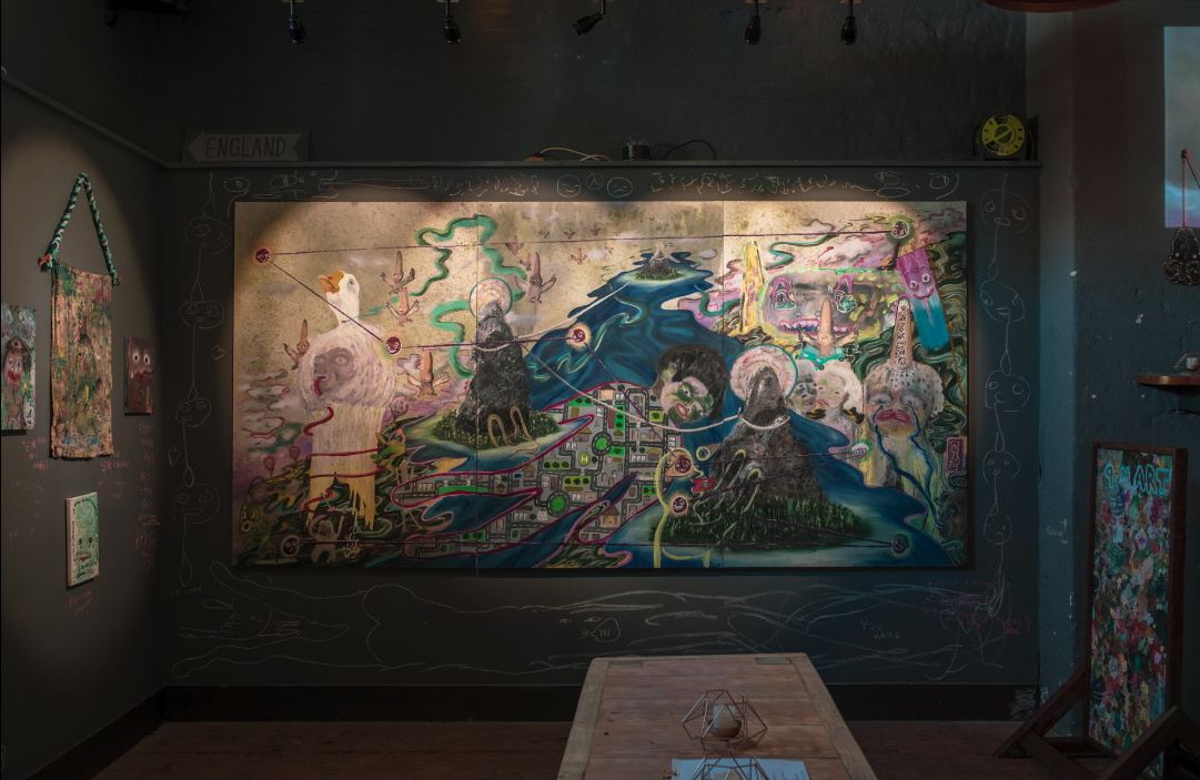 Art installation featuring a colorful, surreal painting with abstract figures, landscapes, and symbols on a wall in a dimly lit room.