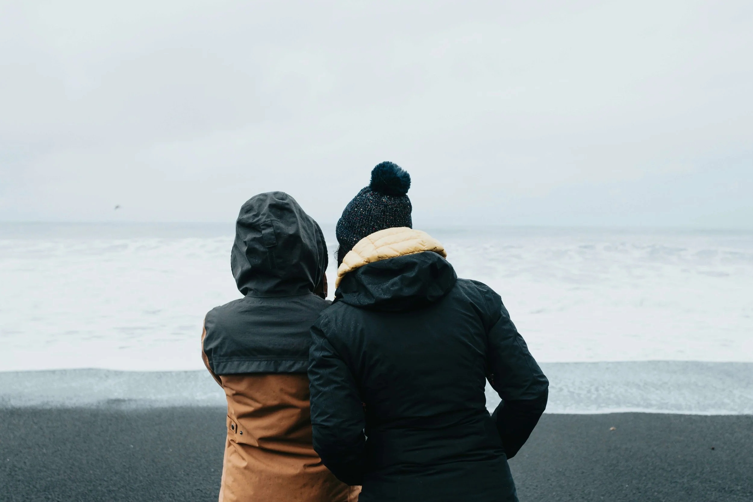 Two people in rain jackets look out to the ocean
