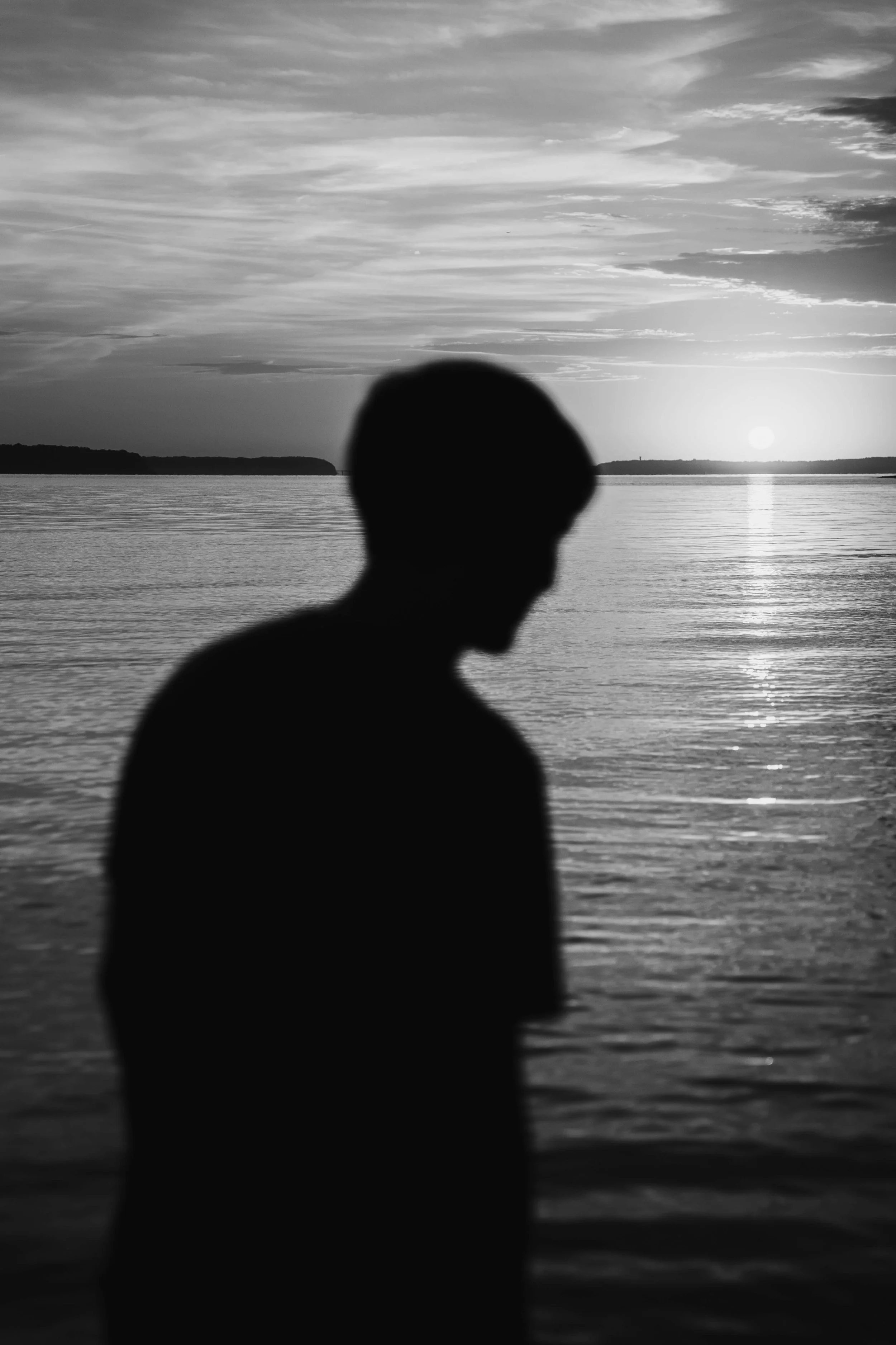 A figure in grayscale is silhouetted in front of a lake