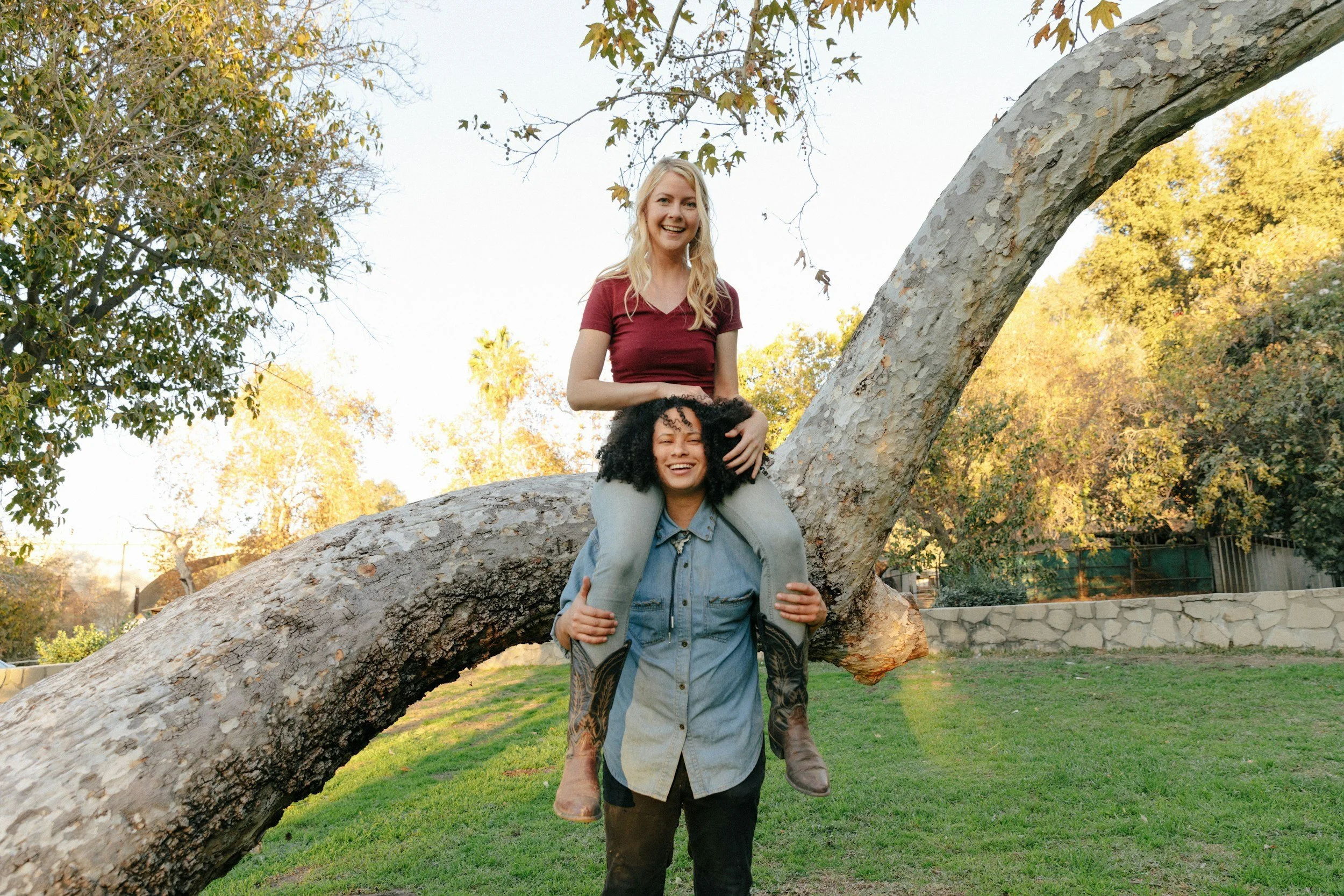 A woman sits on a man's shoulders as he stands in a park