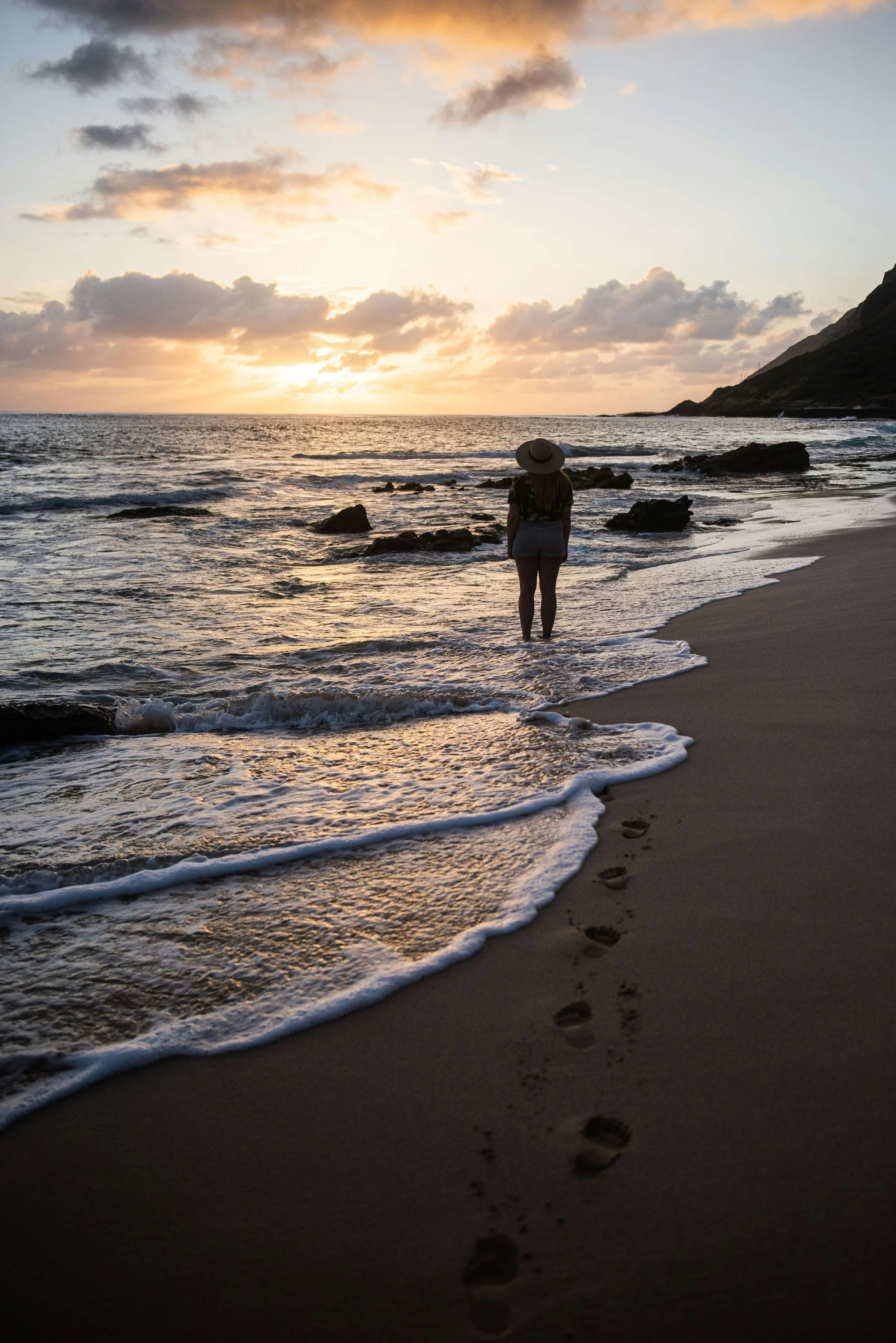 A silhouetted figure stands in the ocean at sunset