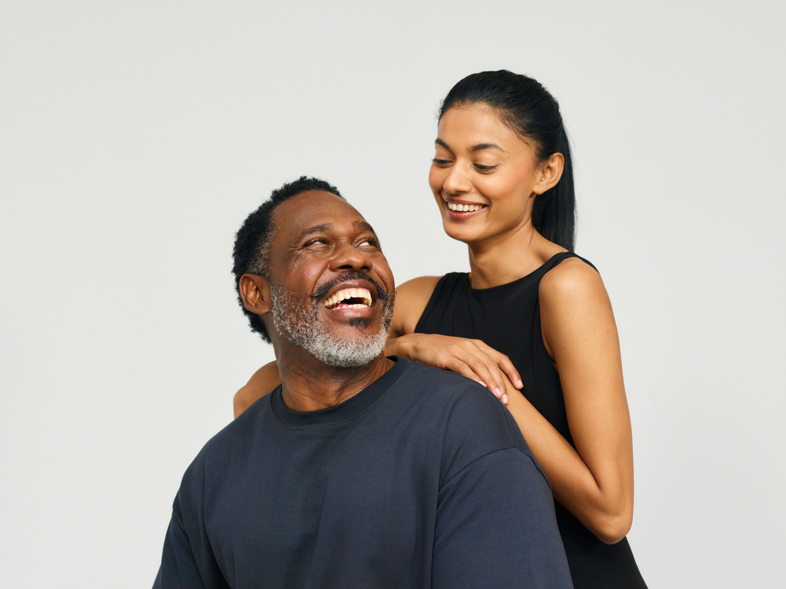 A father and daughter poses in front of a white backdrop, smiling at one another