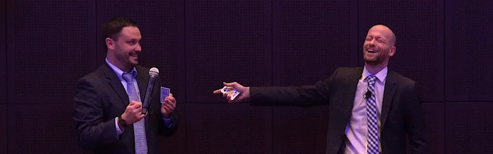 Mentalist Fred Berthelot laughing on stage beside a volunteer from the audience