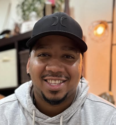 Person in a maroon jacket seated on a bench against a brick wall.
