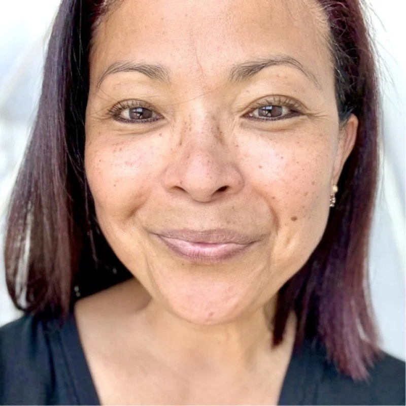 Woman smiling indoors with soft lighting and a dark top