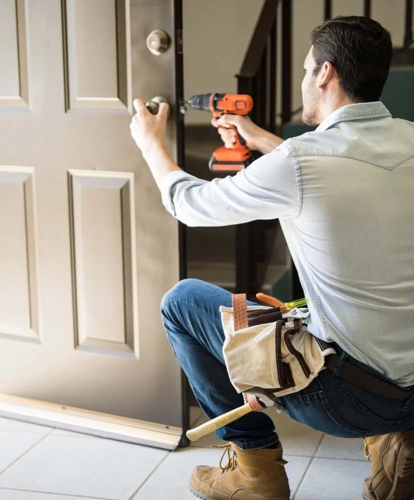 Handyman using a cordless drill to adjust residential door hardware during a small rental turnover repair visit.