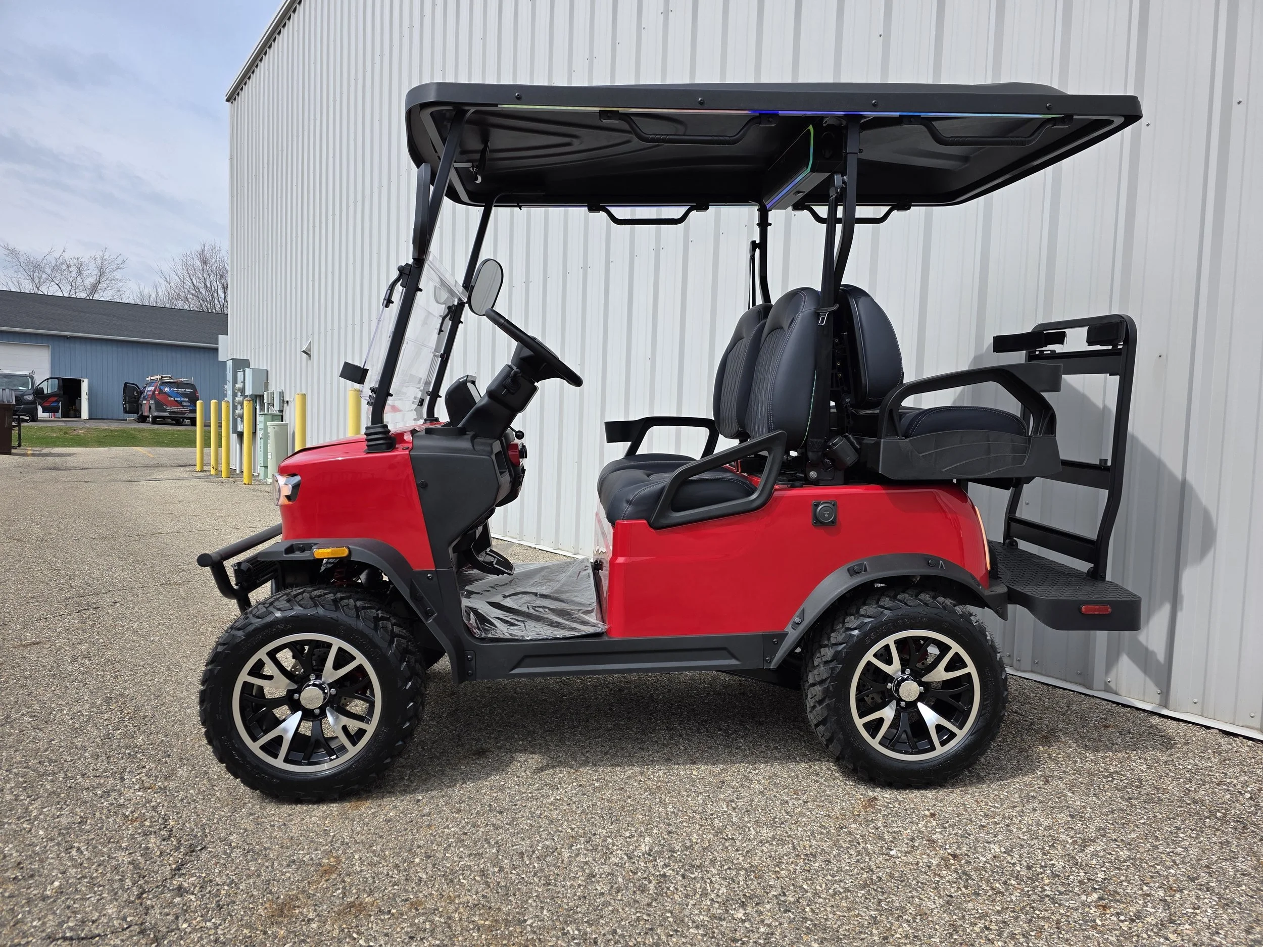 Red and black electric golf cart with four seats, parked outside a building with a white corrugated metal wall.