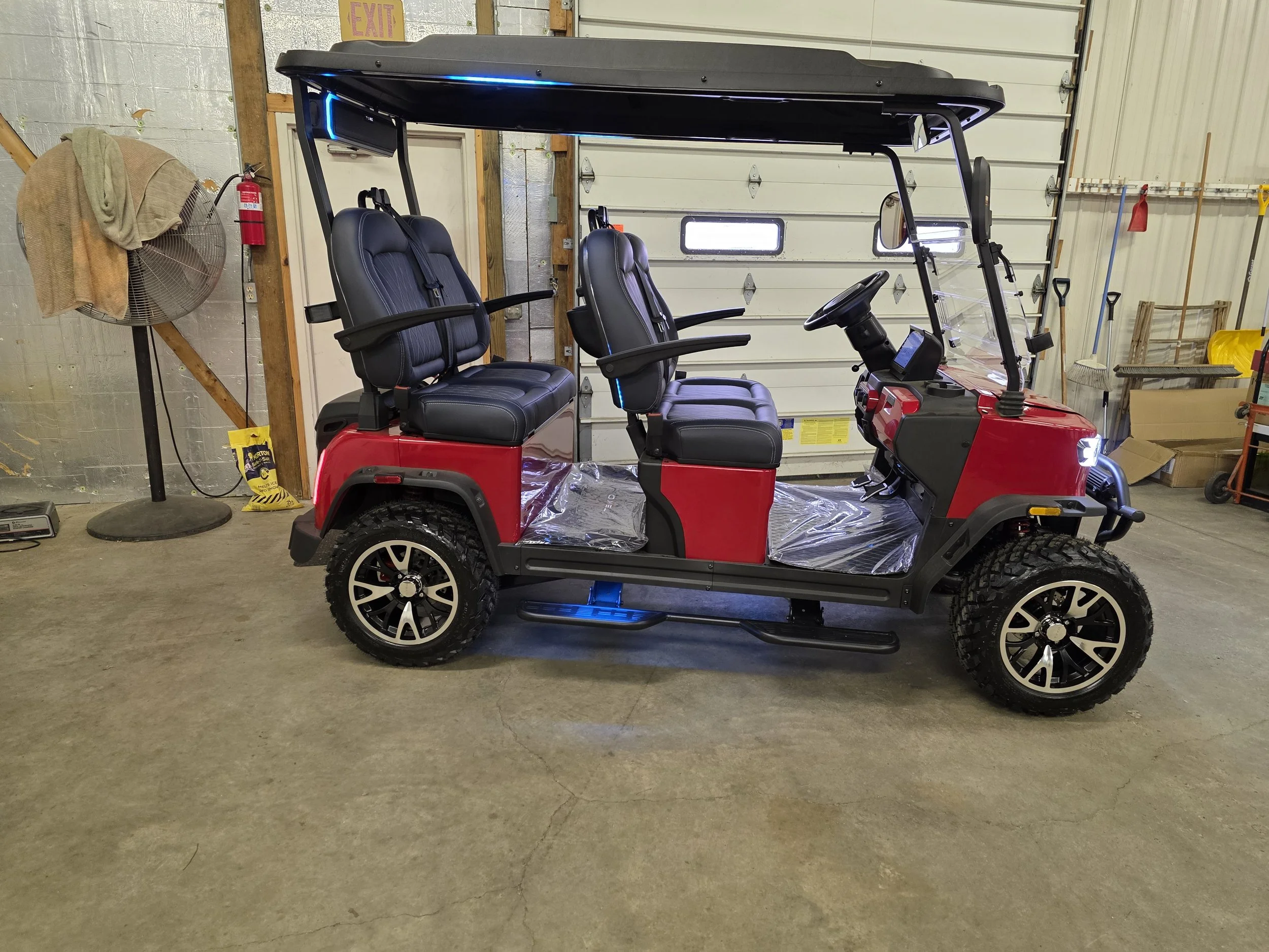 Red electric golf cart with four black seats inside a garage.