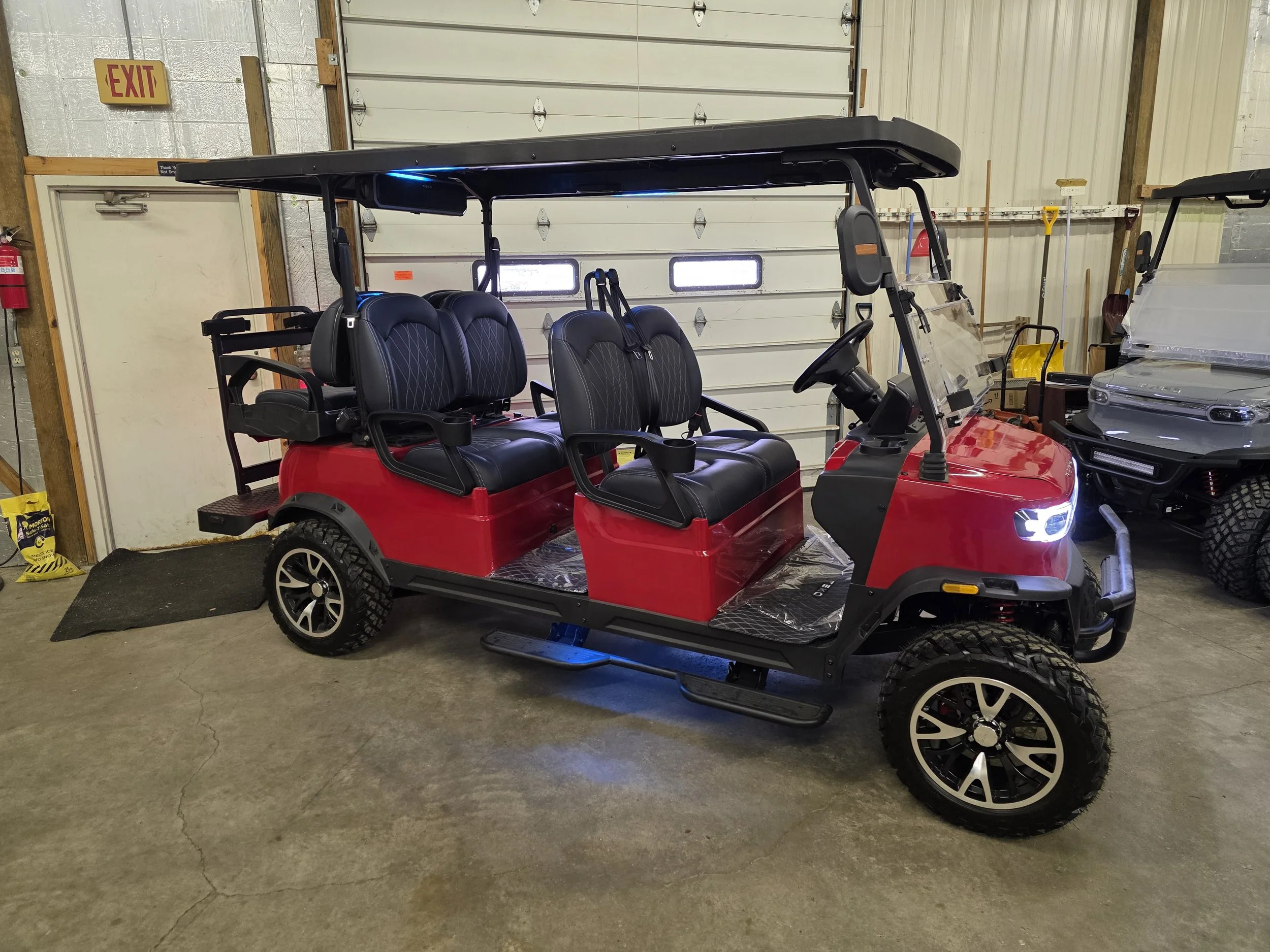 A red four-seater golf cart inside a garage with white walls, a closed garage door, and tools hanging on the wall.