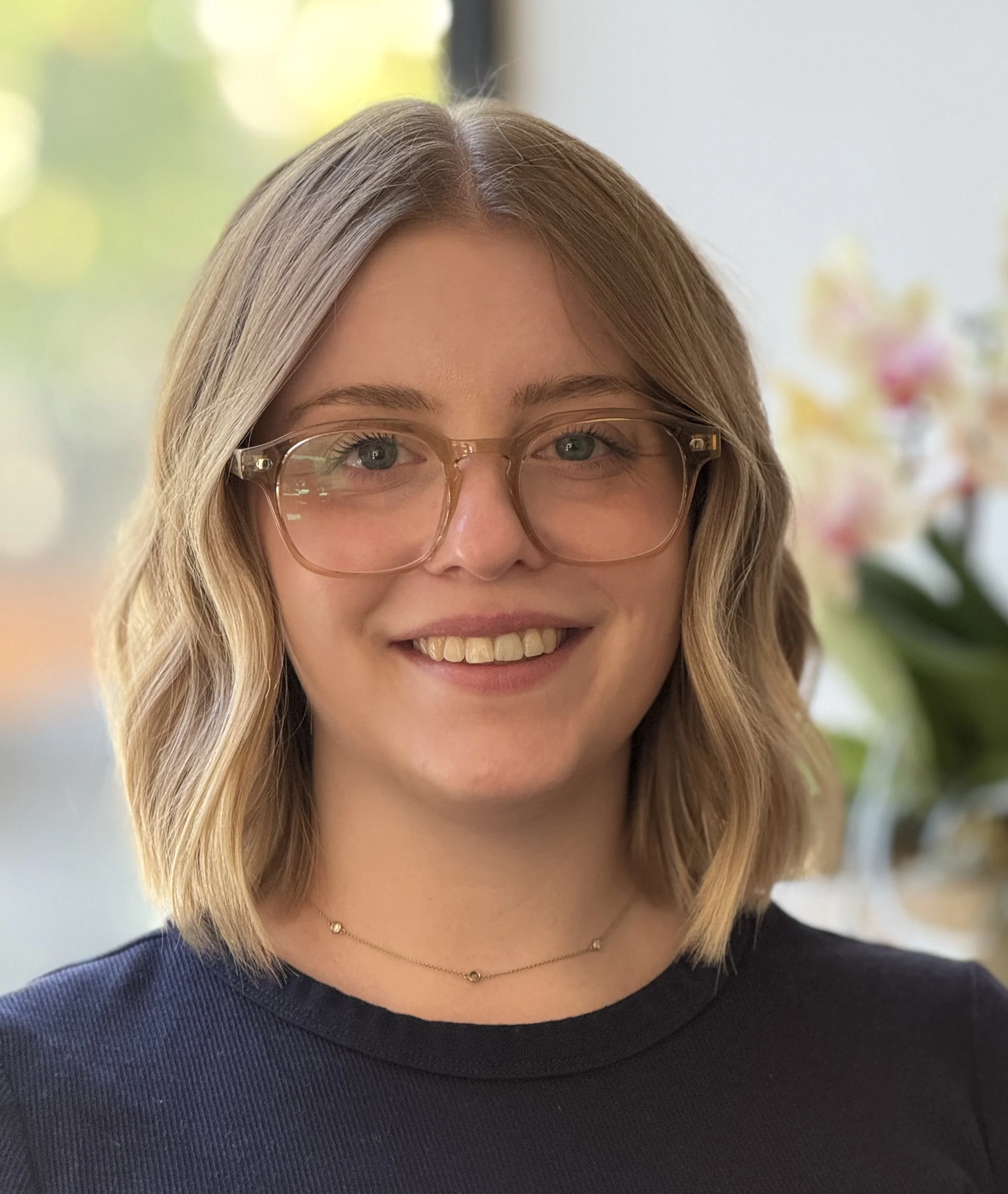 A woman with shoulder-length blonde hair, wearing glasses and a black top, smiling at the camera.