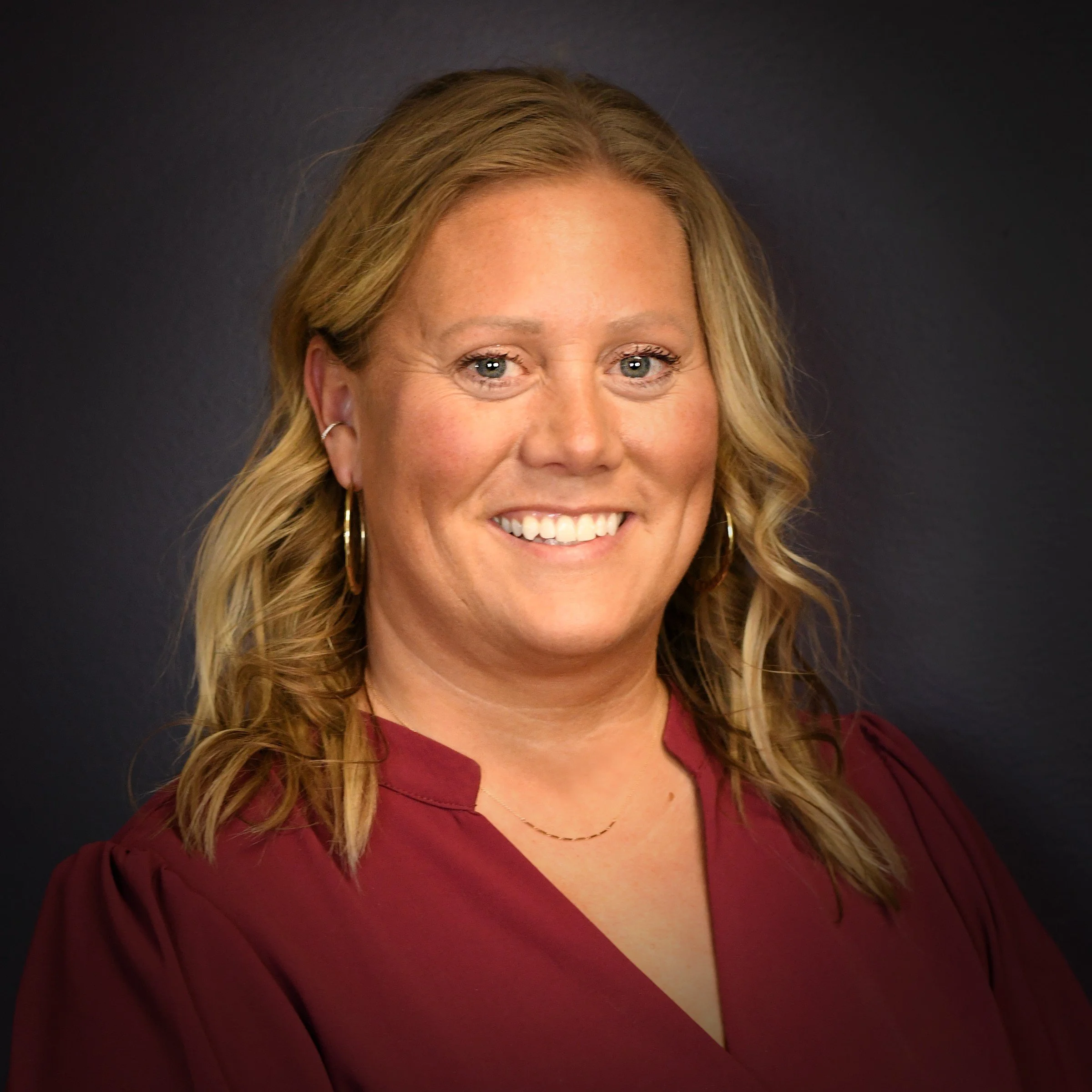 A woman with blonde hair smiling, wearing a red top