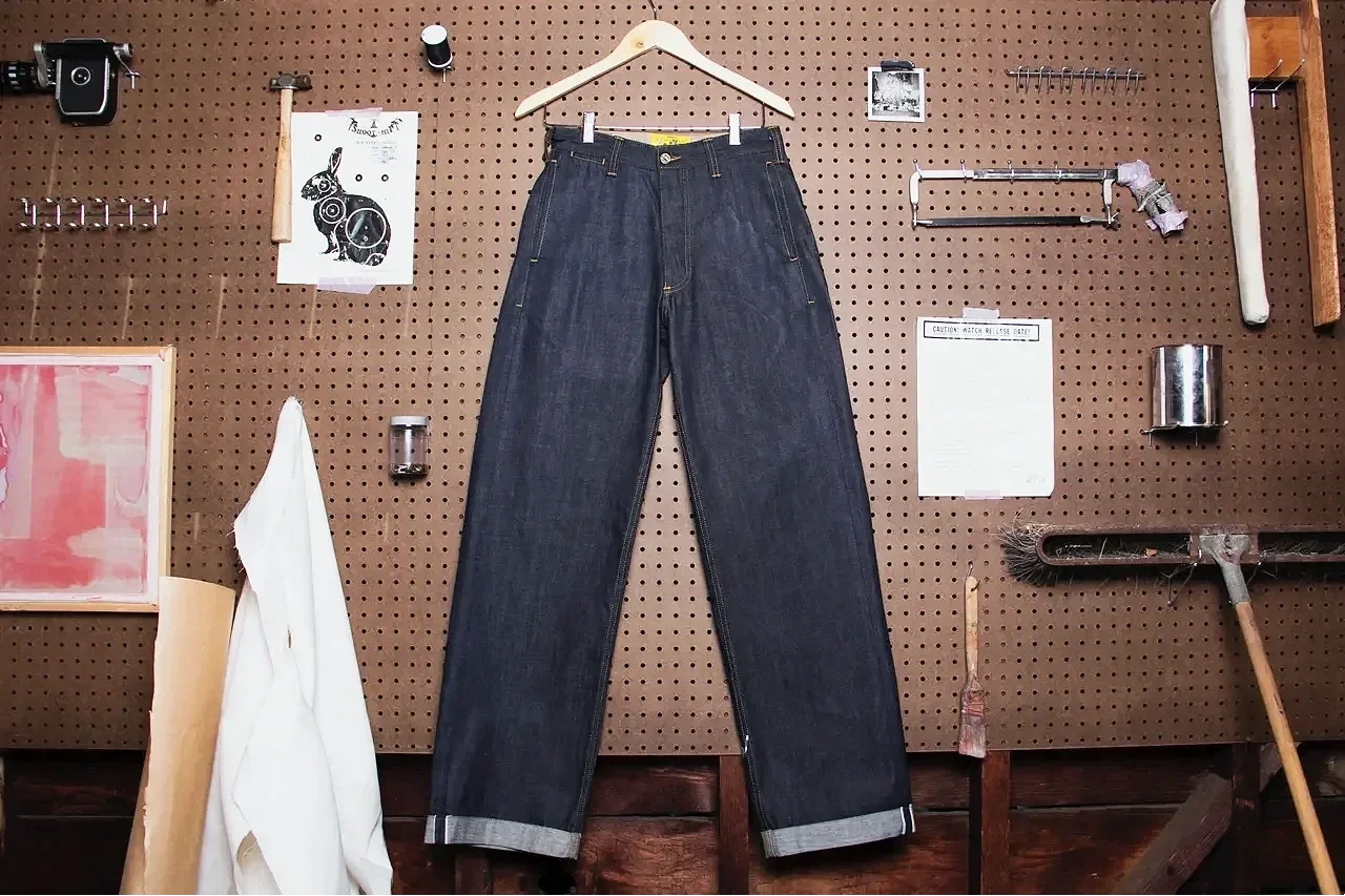 A pair of dark denim jeans hung on a pegboard in a workshop or art studio, surrounded by tools and art supplies.