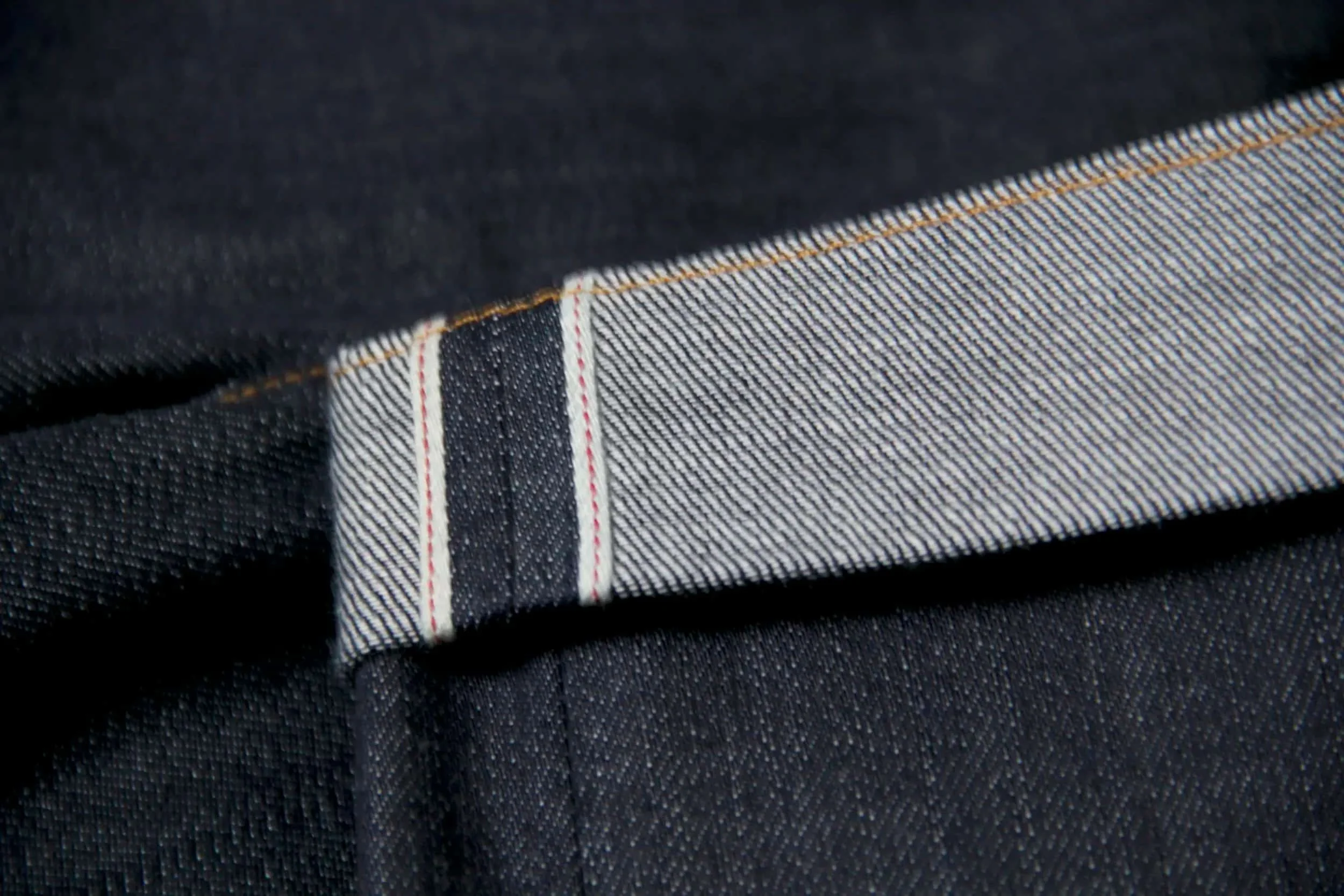 Close-up of a dark fabric with a visible seam and detailed stitching, possibly denim or similar material.
