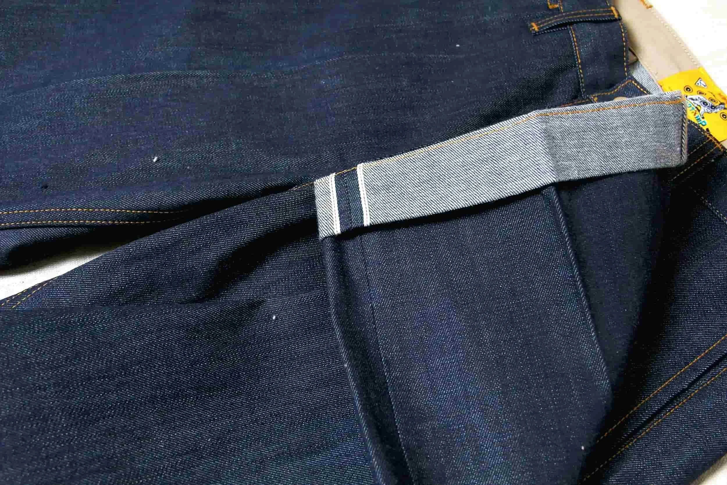 Close-up of dark blue denim jeans with contrasting stitching and a partially visible yellow tag.