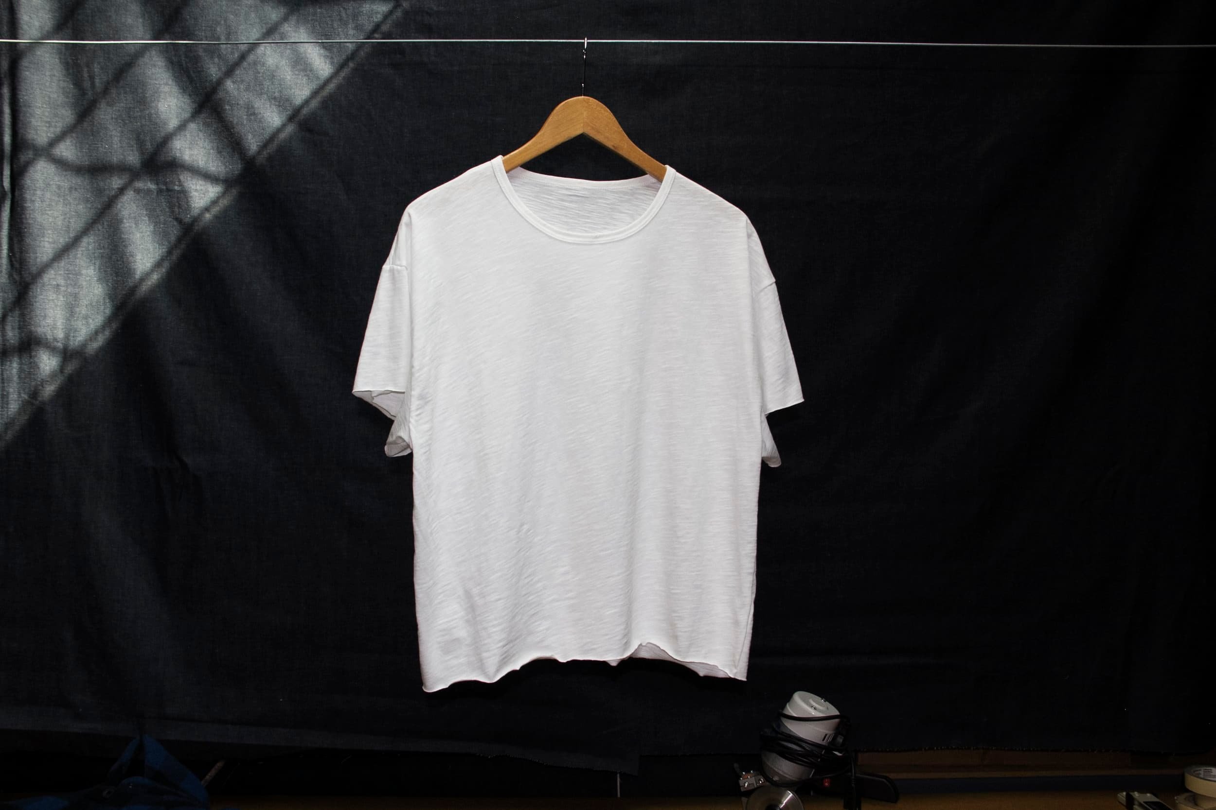 A plain white T-shirt hanging on a wooden hanger against a dark background.