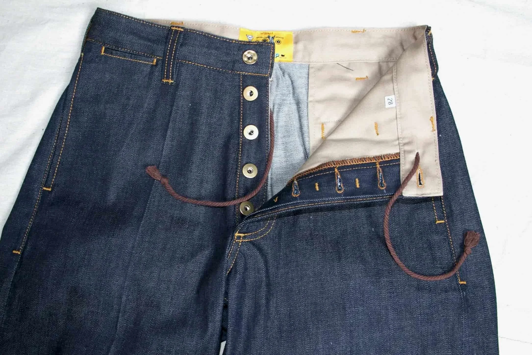 Dark blue denim jeans partially unzipped and unbuttoned, showing the inner lining and a yellow tag inside.