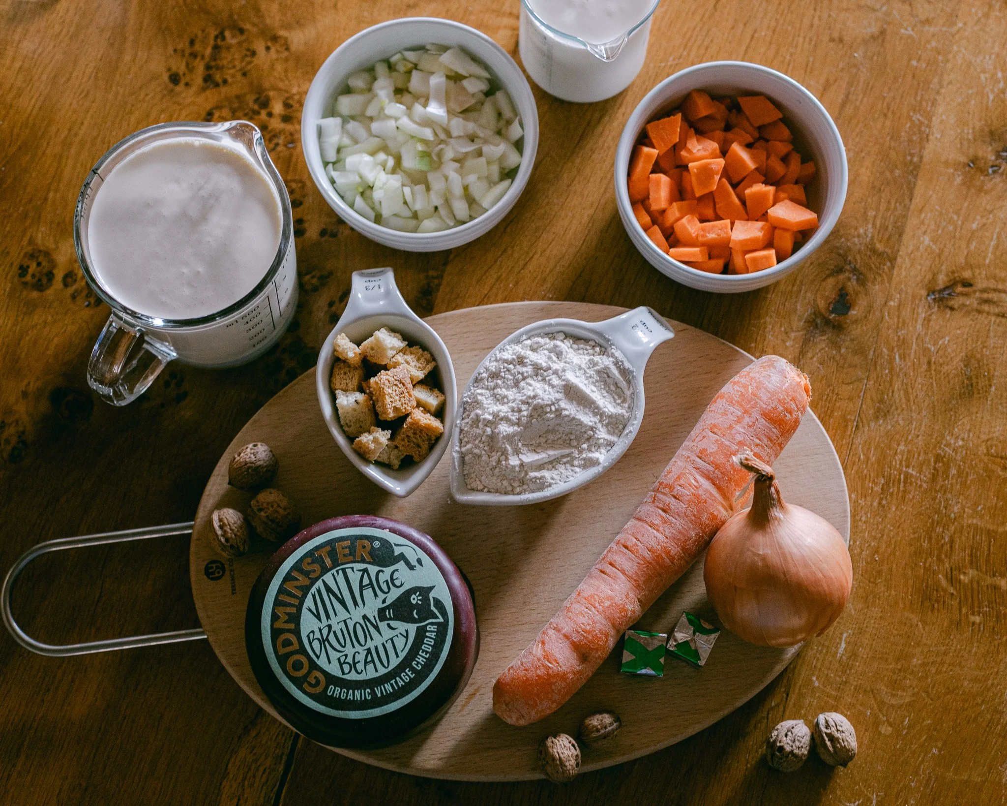Ingredients gathered for cooking a declius cheese soup, including a block of Godminster Vintage Cheddar, a carrot, and onion, croutons, flour, and cream.