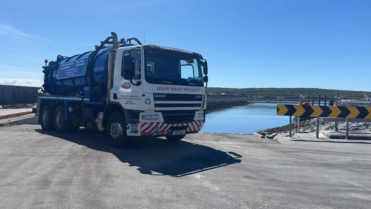 Liquid waste disposal truck parked near a scenic body of water with clear blue sky in the background.