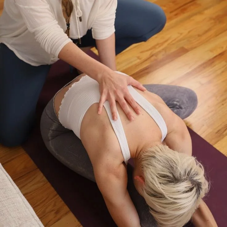 Aula particular de yoga. Pessoa a ajudar outra numa alongamento de ioga no tapete.