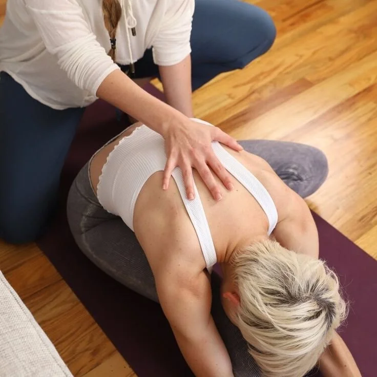 Aula particular de yoga. Pessoa a ajudar outra numa alongamento de ioga no tapete.
