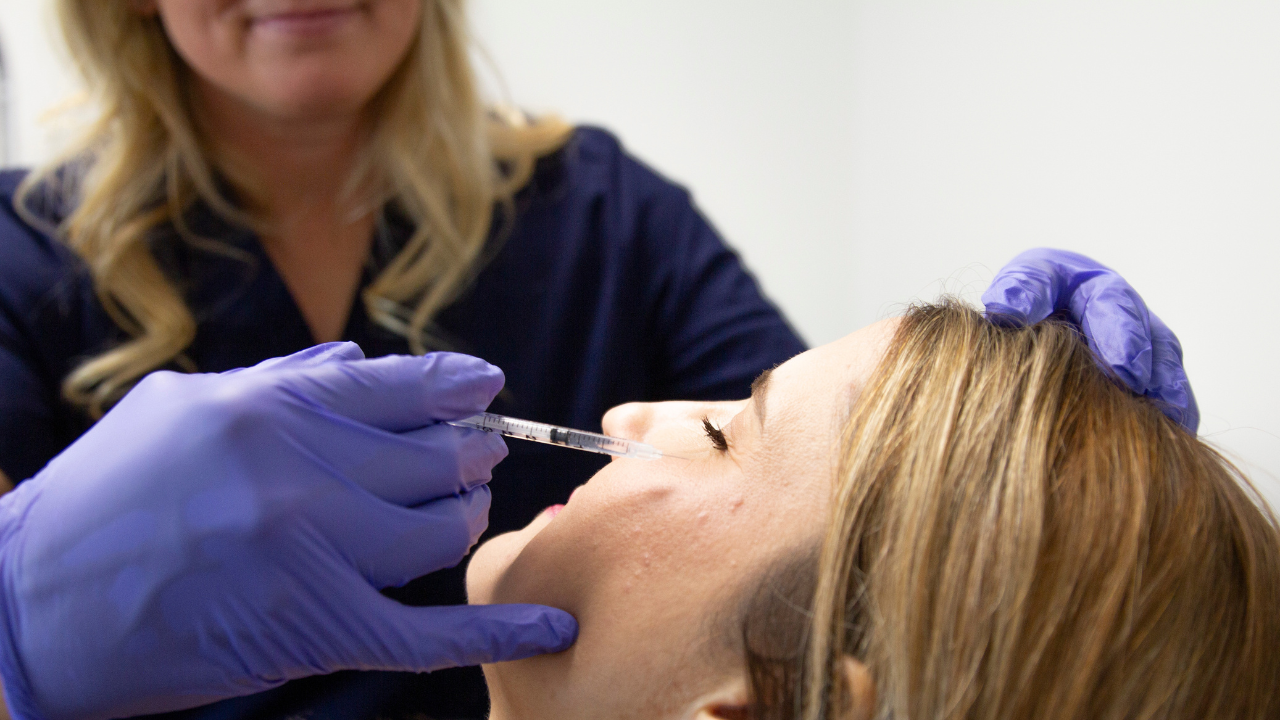 A woman receiving a laser facial treatment called Moxi, wearing protective goggles, applied by a person with gloves.