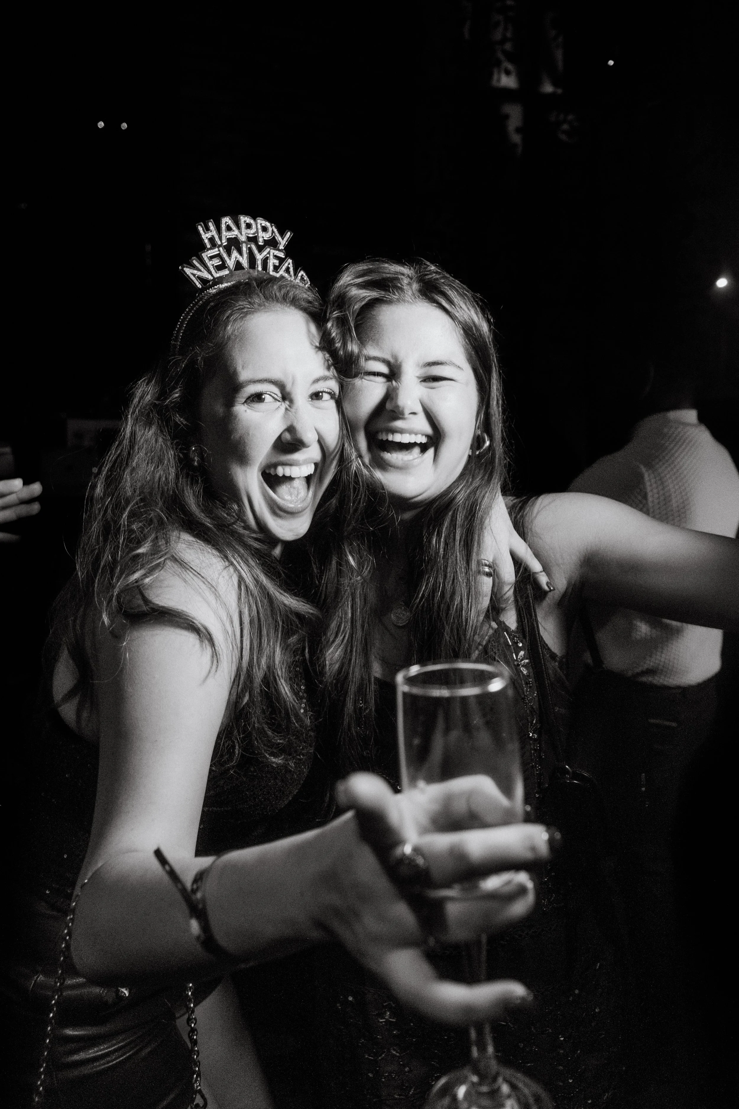 Two women celebrating New Year's Eve, smiling and holding a glass of champagne at a party.