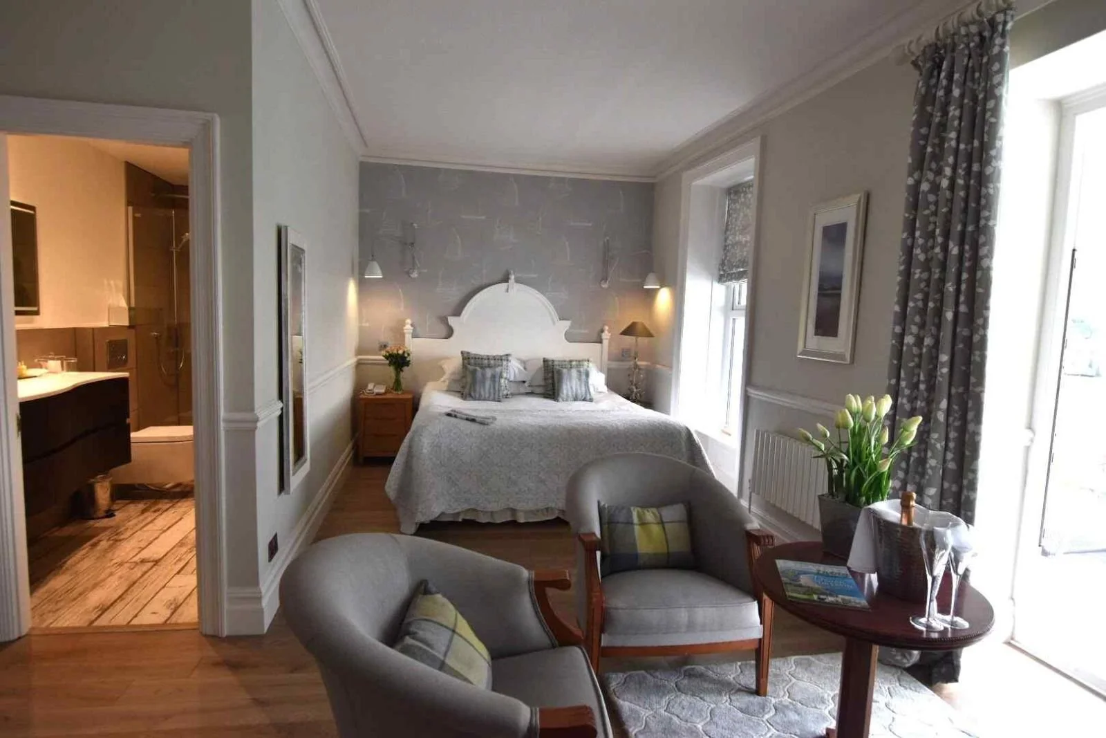 Luxury hotel bedroom with a double bed, seating area, balcony doors, and an en suite bathroom at Watersmeet Hotel overlooking the coast.