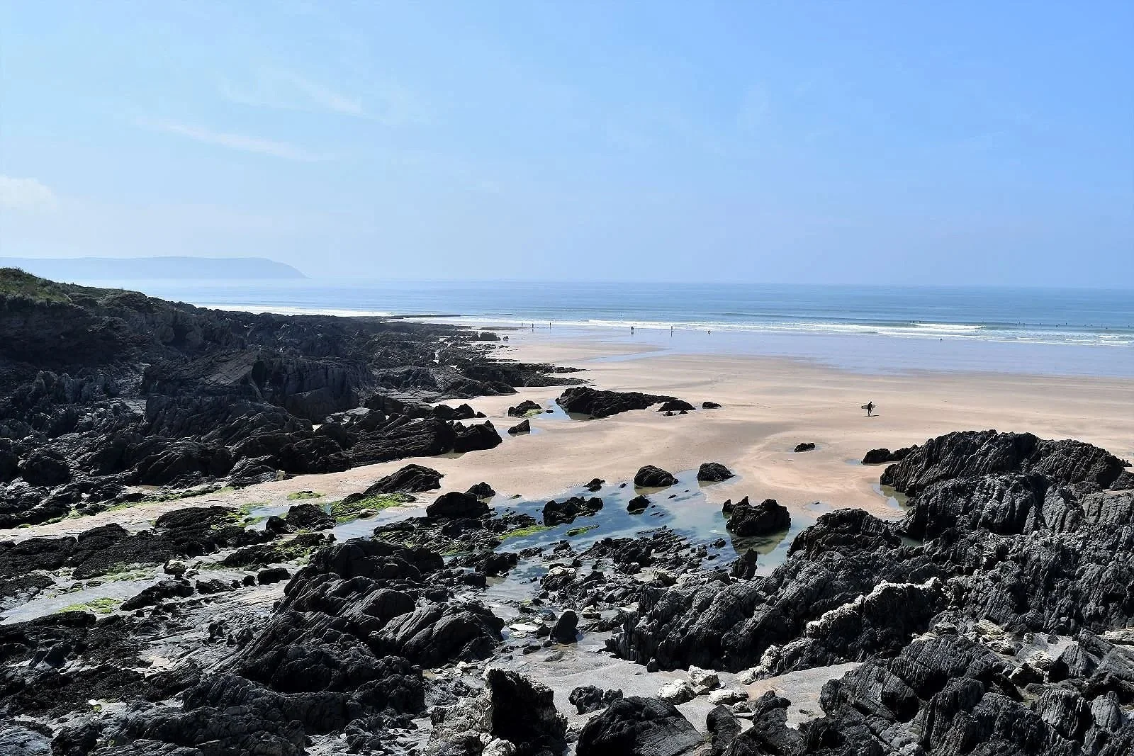 Rocky shoreline at Combesgate Beach with golden sand, clear blue sea and coastal cliffs on a sunny day in Woolacombe, North Devon.