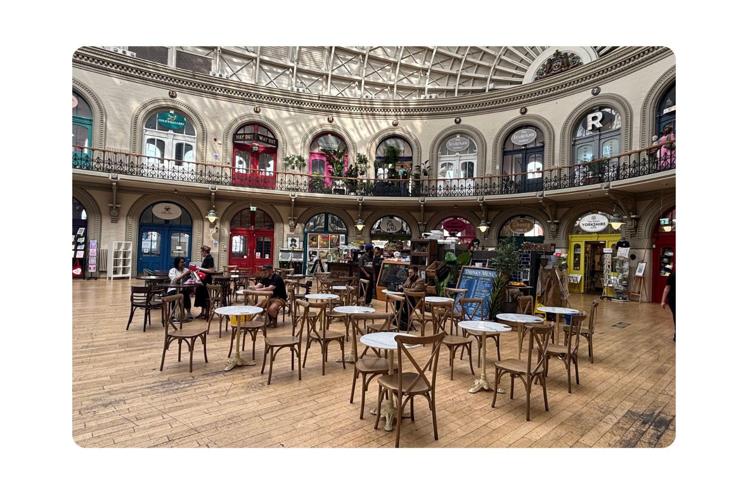 A shopping scene. A wall of arches, each holding a different storefront. In the from of the wall a large space with tables and chairs.