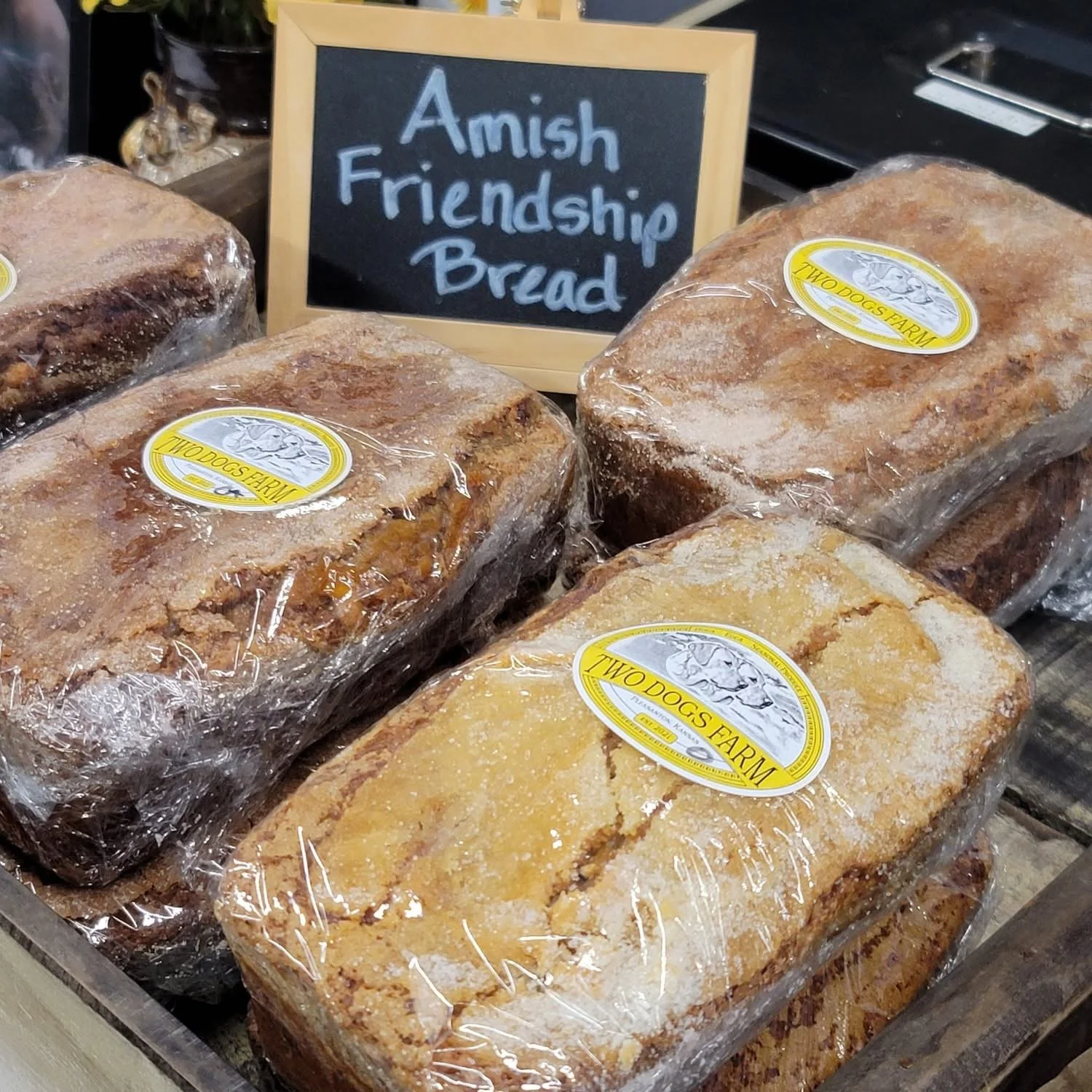 Several blocks of Amish Friendship Bread in plastic wrap on a display table, with a sign in the background that reads 'Amish Friendship Bread'.